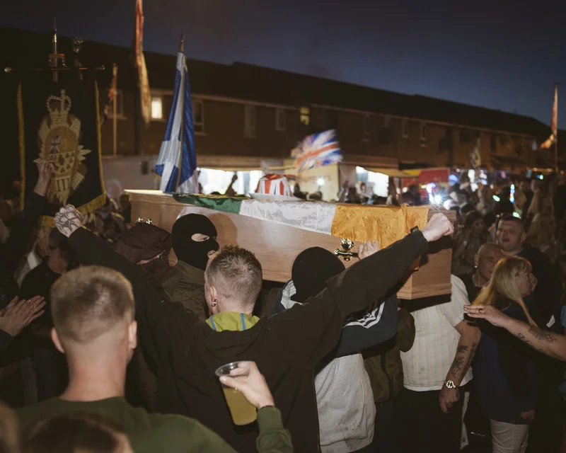 A coffin with the Irish flag is transferred by Loyalist paramilitary youth to be burned at a huge bonfire next to the so-called peace wall interfacing with Catholic Irish Republican neighbourhood of Falls. As a yearly Protestant ritual, 11th Night bonfires are preceding Orange Order marches on Twelfth of July. The event is discussed highly controversial between the opposing communities in Northern Ireland, Protestant Loyalist Upper Shankill area, Belfast
