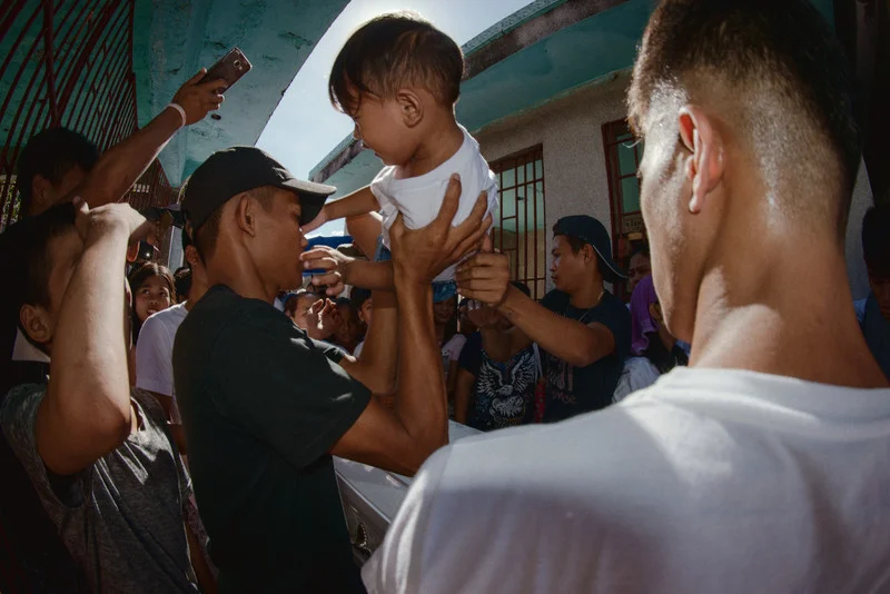 Young relatives and children of the deceased, Jovito Marquez Jr, are carried over his casket and cadaver before entombment in La Loma Cemetery to hinder the ghost of the dead relative from visiting the children. On November 5 at around 5 am, two unidentified bodies were found, one along R 10 in Navotas and the other at Tanigue St. under the Sawata bridge along C3. Both had single shots on the head and both victims had strangulation marks around their necks and cuff marks on their wrist. One of them was later identified as Jimboy Opriasa, 35 years old, a resident of Gensan St. Sangandaan, Caloocan. The other was identified as Jovito Marquez Jr. 23 years old, a resident of Malaya, St. Balut, Tondo. Both deaths mark another case in the growing list of extrajudicial killings and forced disappearances that began during President Duterte's War on Drugs in 2016. CALOOCAN, MANILA. 2018.