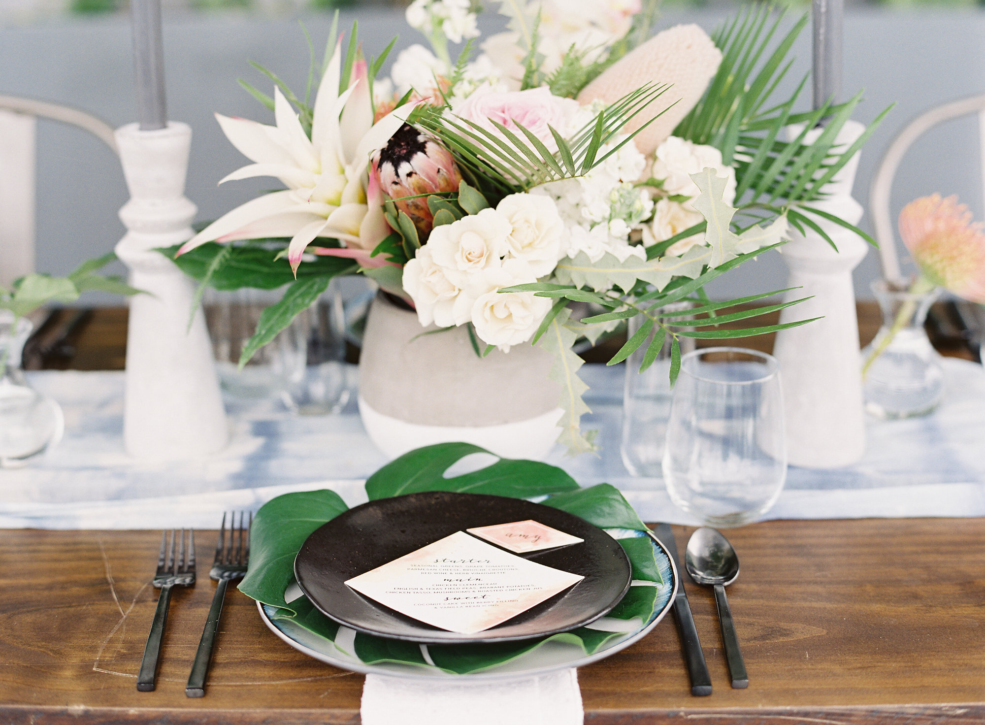 Soft blues mixed with black china, brushed metal flatware and opulent tropical floral makes for a wining combintation. 