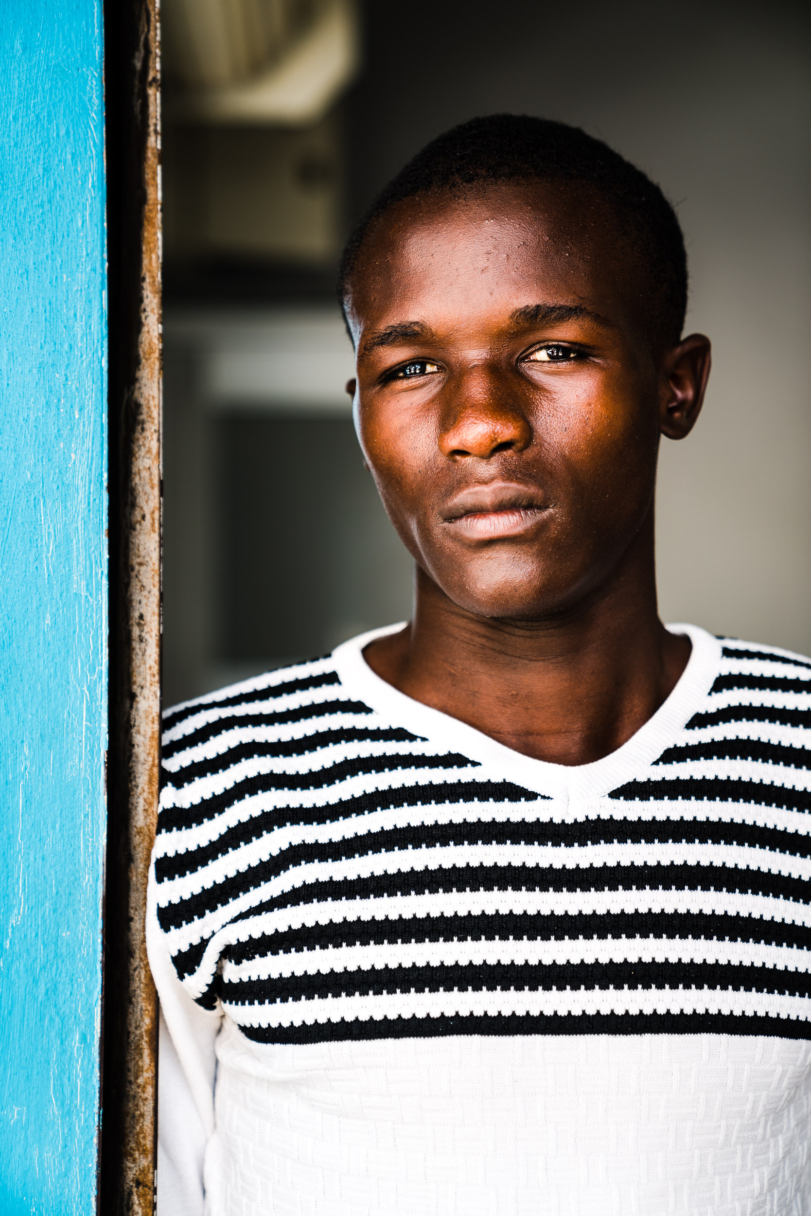 A young man watches from a doorway. Higüey, Dominican Republic. 2018