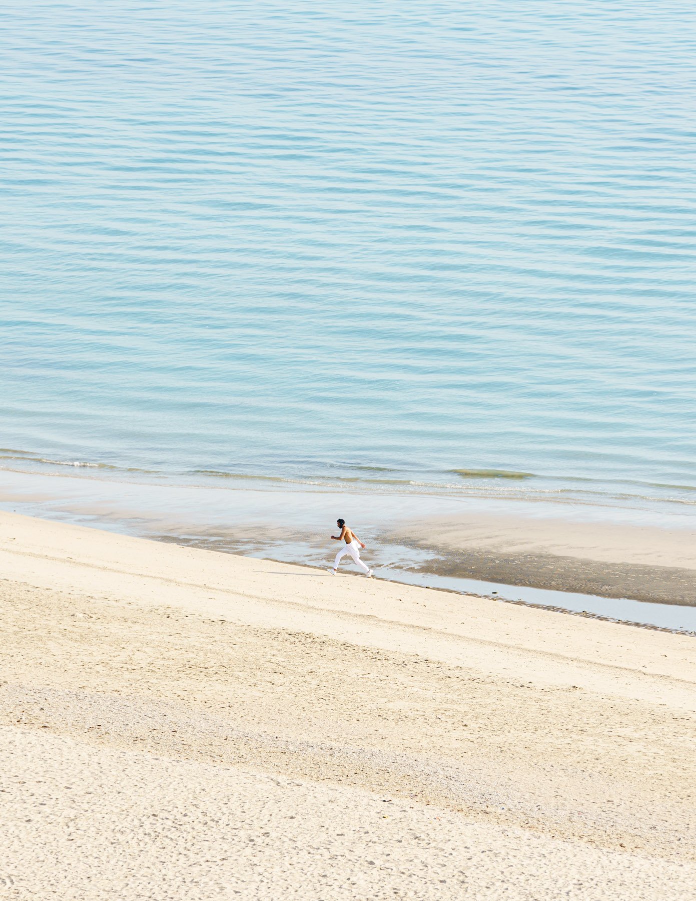  A man jumps over a puddle of sea water.   Salmiya, Kuwait. 2021 