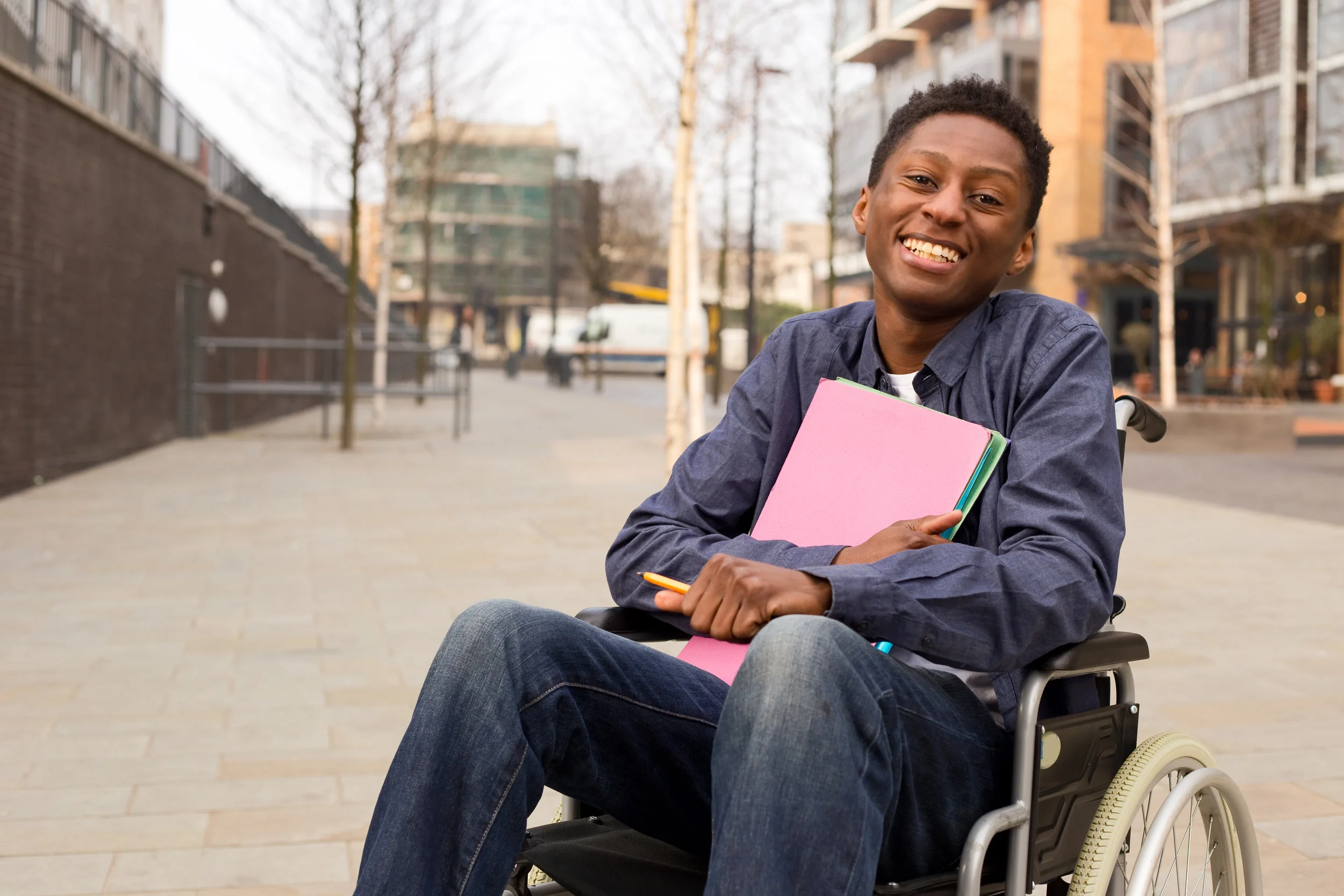 Happy young disabled man in a wheelchair holding folders.