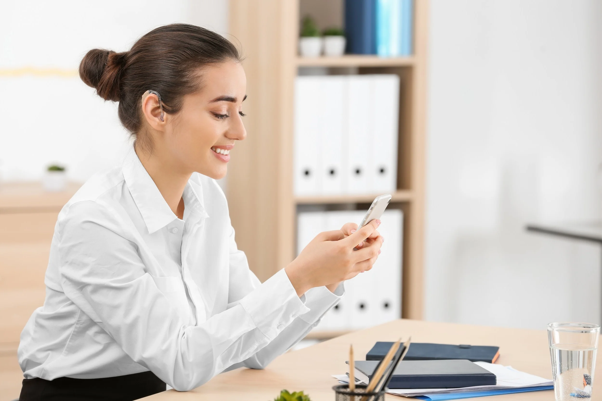 Young woman with hearing aid using smartphone indoors.