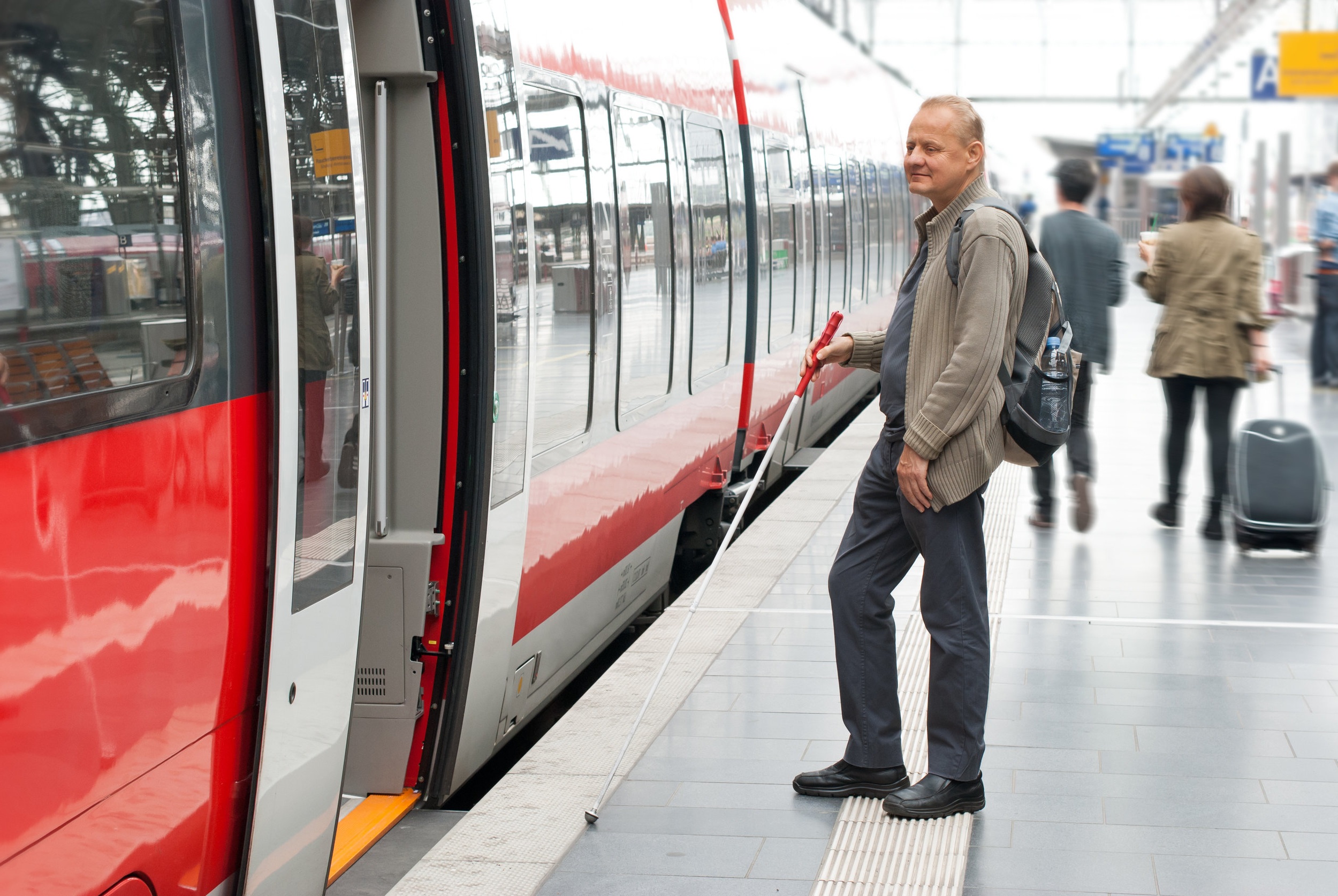 Visually impaired man boarding a train at the station.
