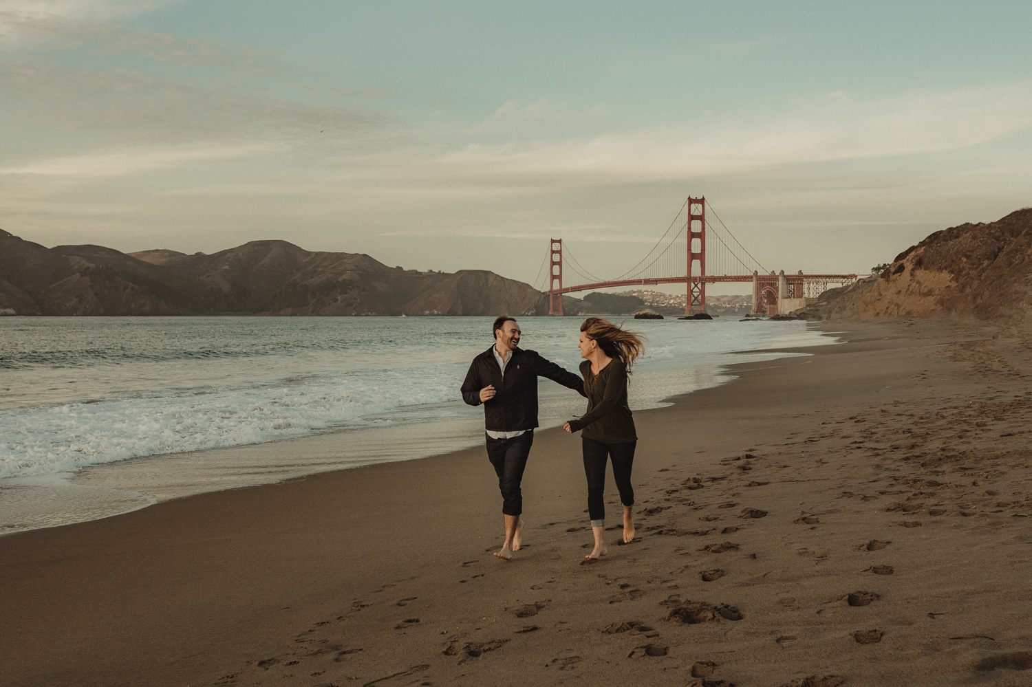 San Francisco engagement couple running at Baker Beach with the Golden Gate in the background photo