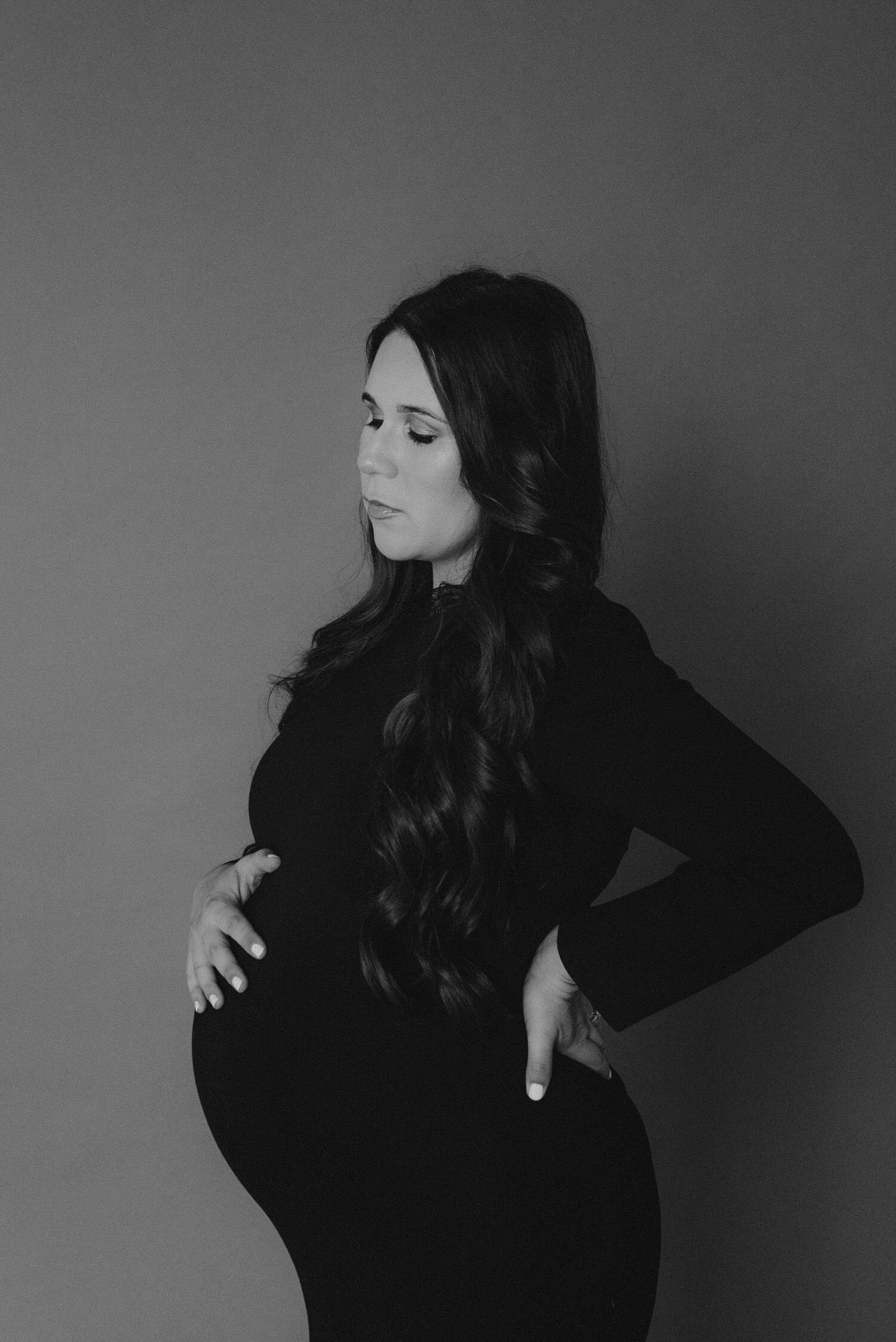 Studio Maternity Session in Reno, with a white background, photo of mom wearing an elegant black maternity dress from rent the runway