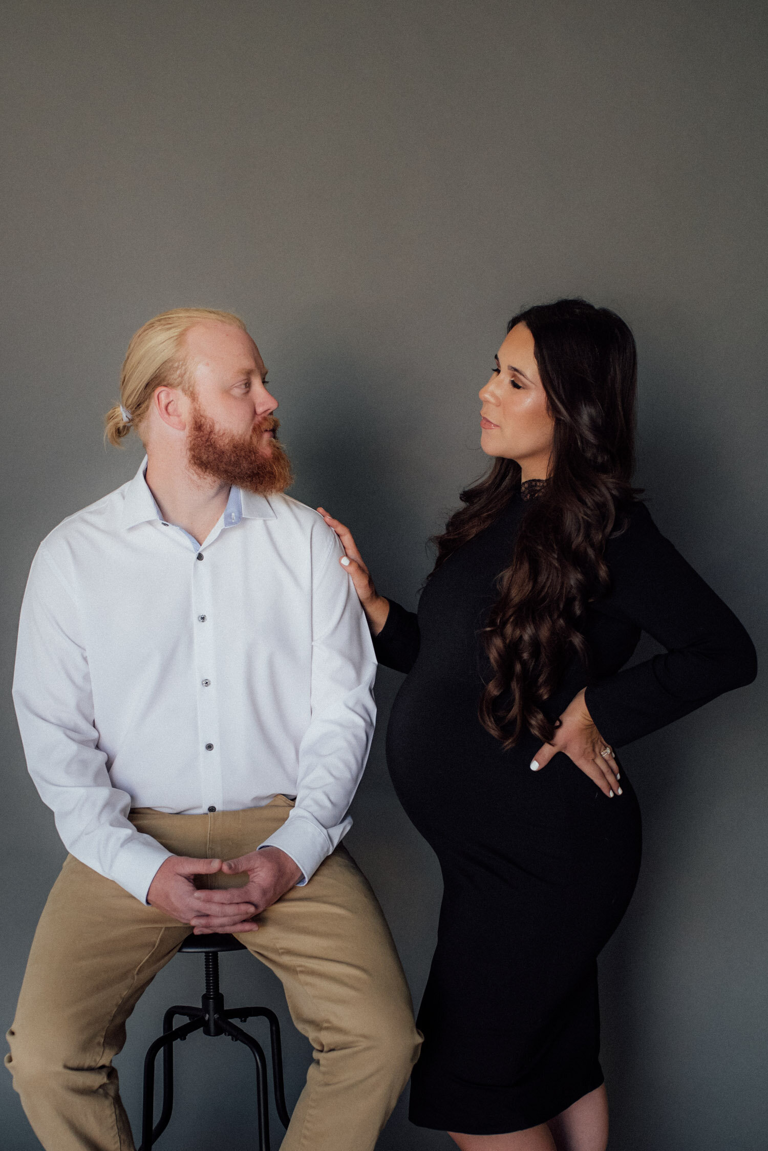 Studio Maternity Session in Reno, with a white background, photo of couple standing in front of a gray studio background