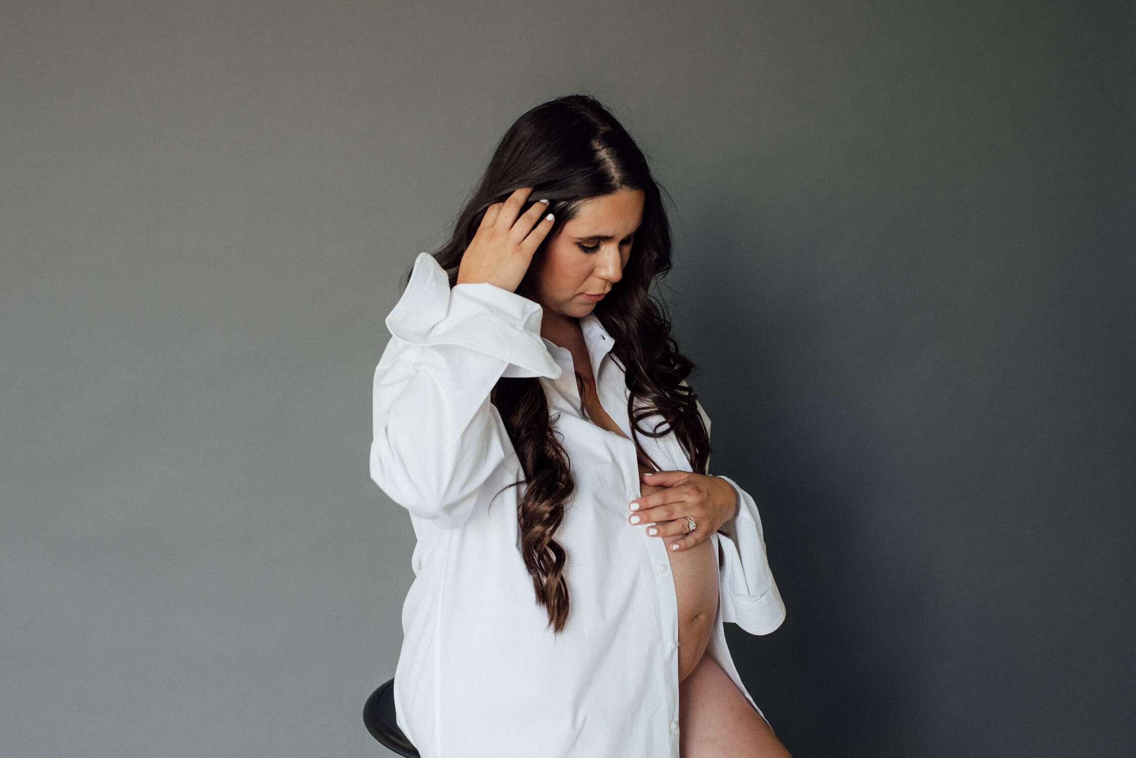 Studio Maternity Session in Reno, with a white background, photo of mom wearing a dressy white maternity shirt that shows off her belly