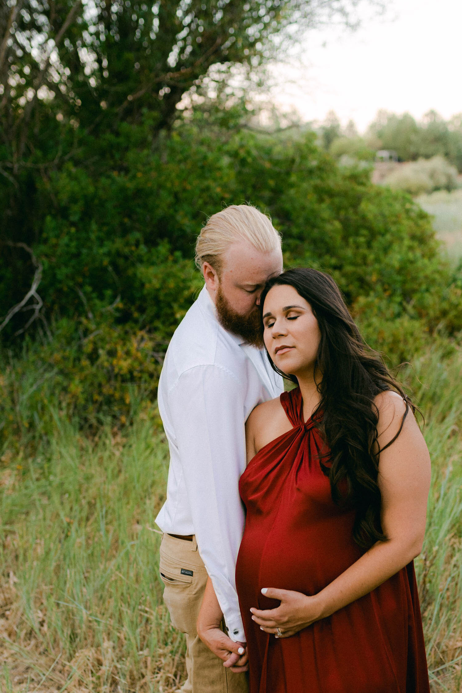 Golden hour maternity session, mom to be is wearing a red gown from rent the runway