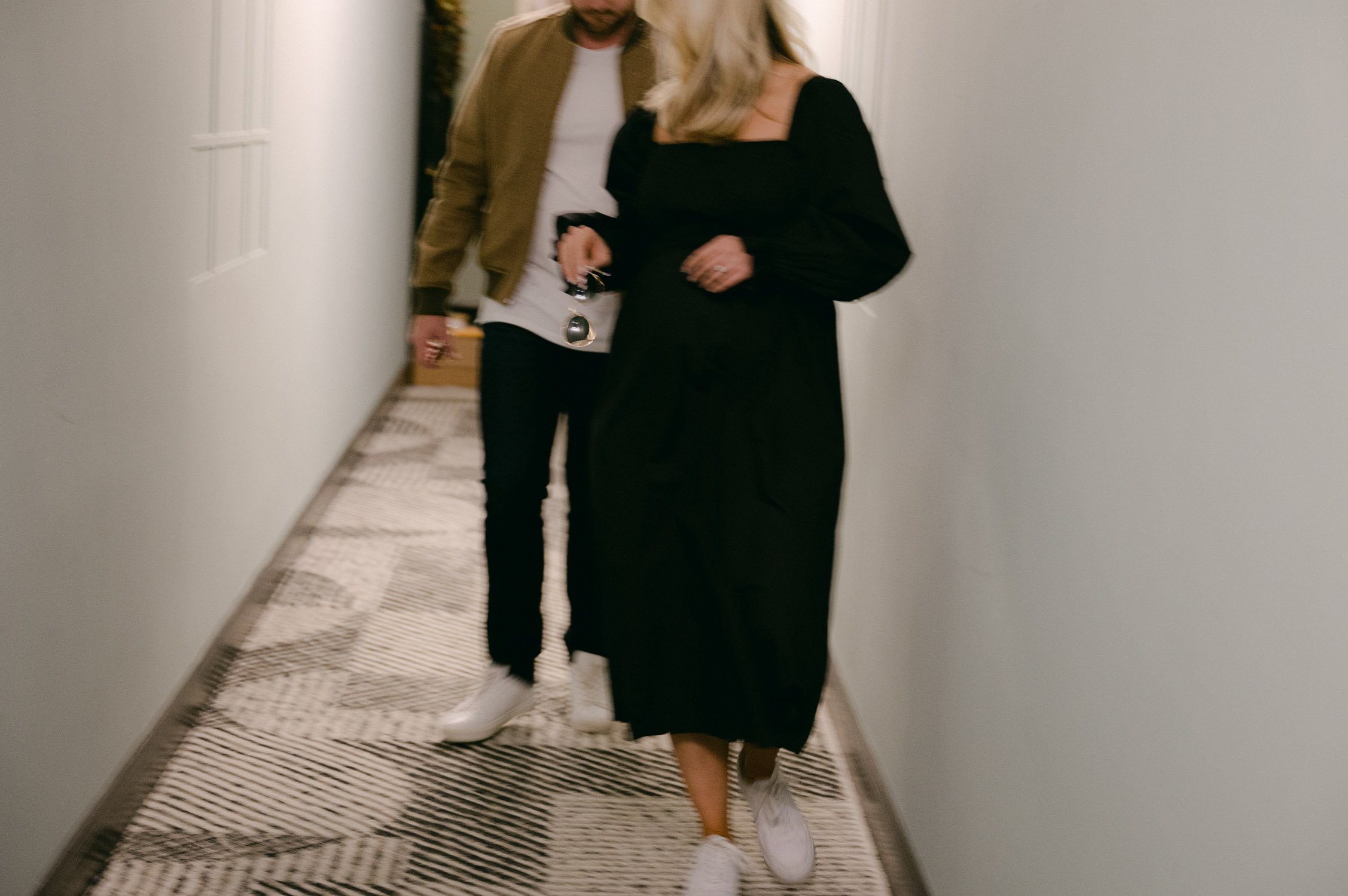 san francisco maternity session, photo of couple leaving their apartment, mom-to-be is wearing a black dress with white tennis shoes and dad is wearing a tan jacket.
