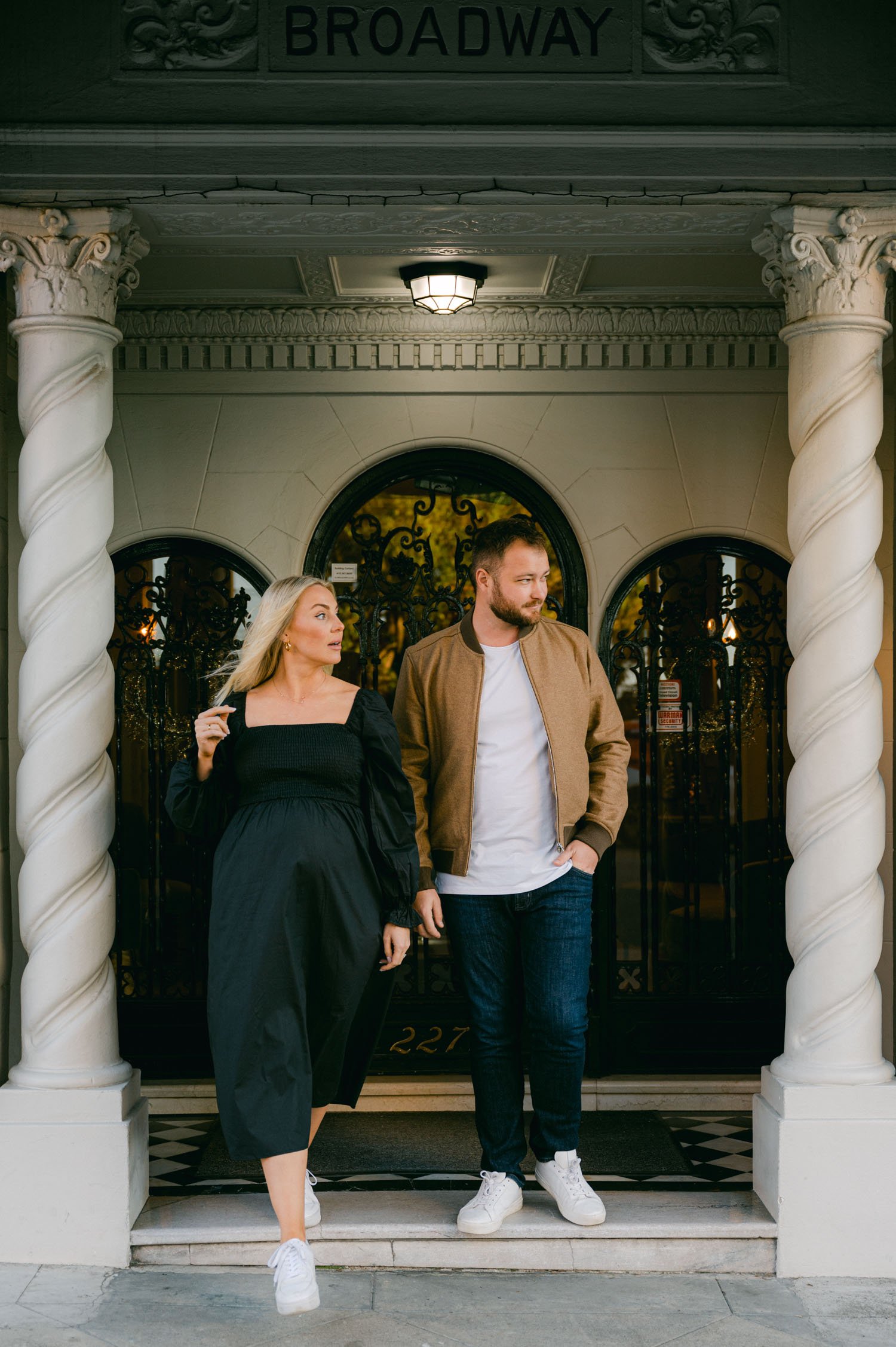 san francisco maternity session, photo of couple holding hands. mom is wearing a black dress with white tennis shoes and dad is wearing a tan jacket, 