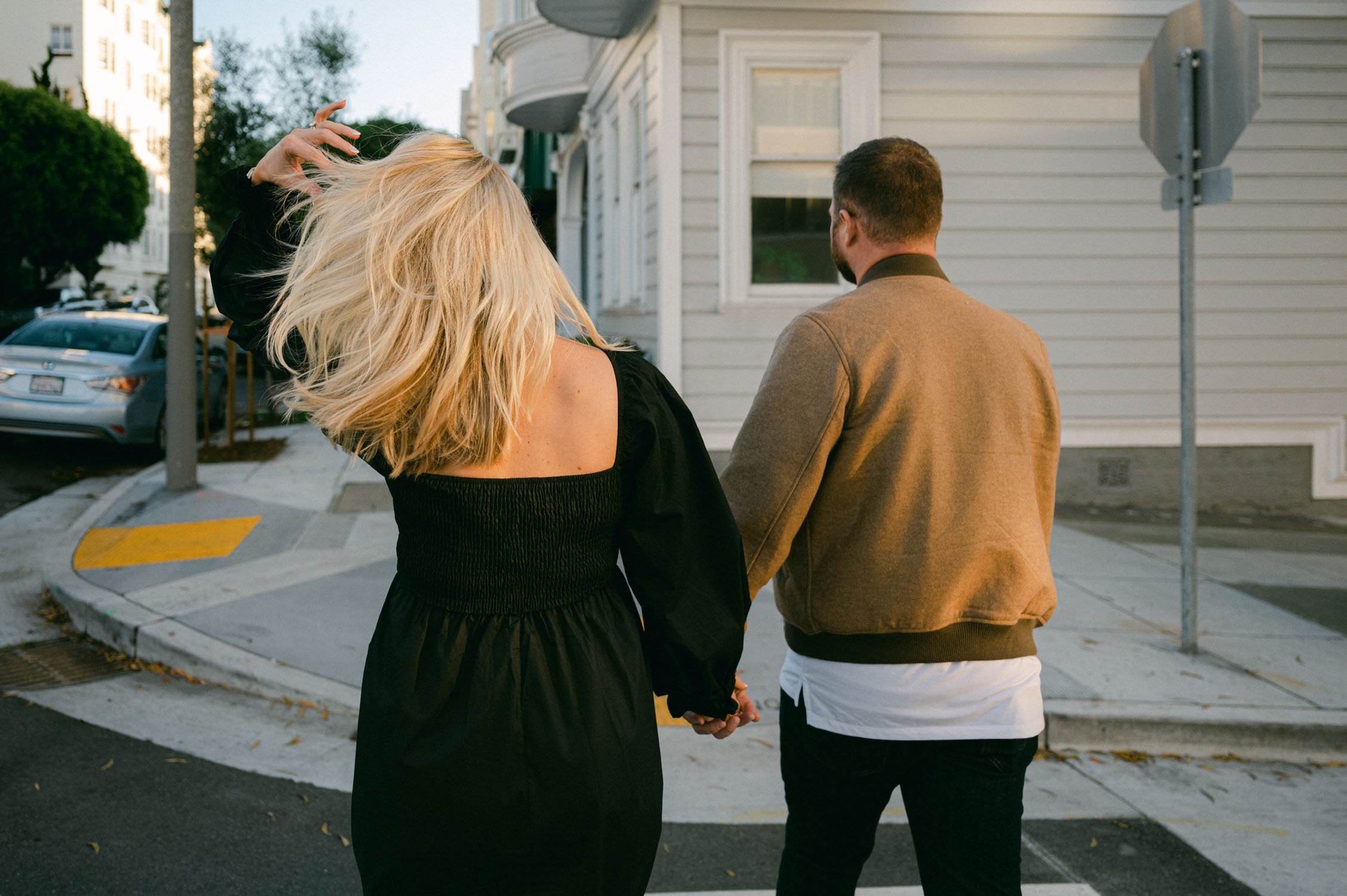 san francisco maternity session, photo of couple holding hands. mom is wearing a black dress with white tennis shoes and dad is wearing a tan jacket