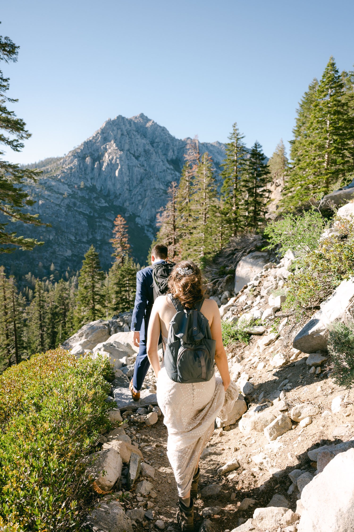 Adventure elopement in Lake Tahoe, photo of couple waking in their wedding attire with backpacks 