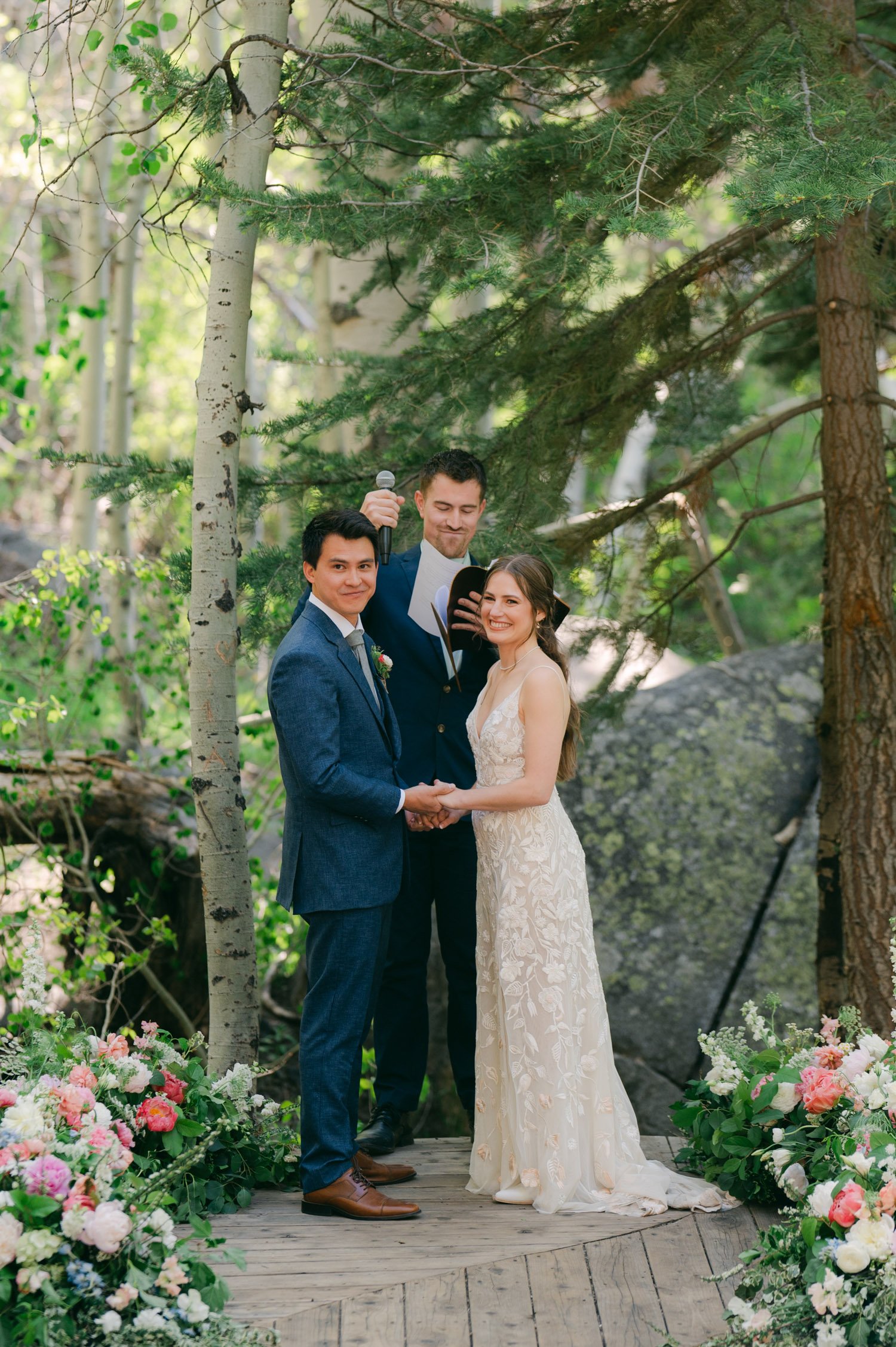 Desolation wilderness hotel wedding, photo of a couple during their wedding ceremony, holding hands, surrounded by flowers in the forest