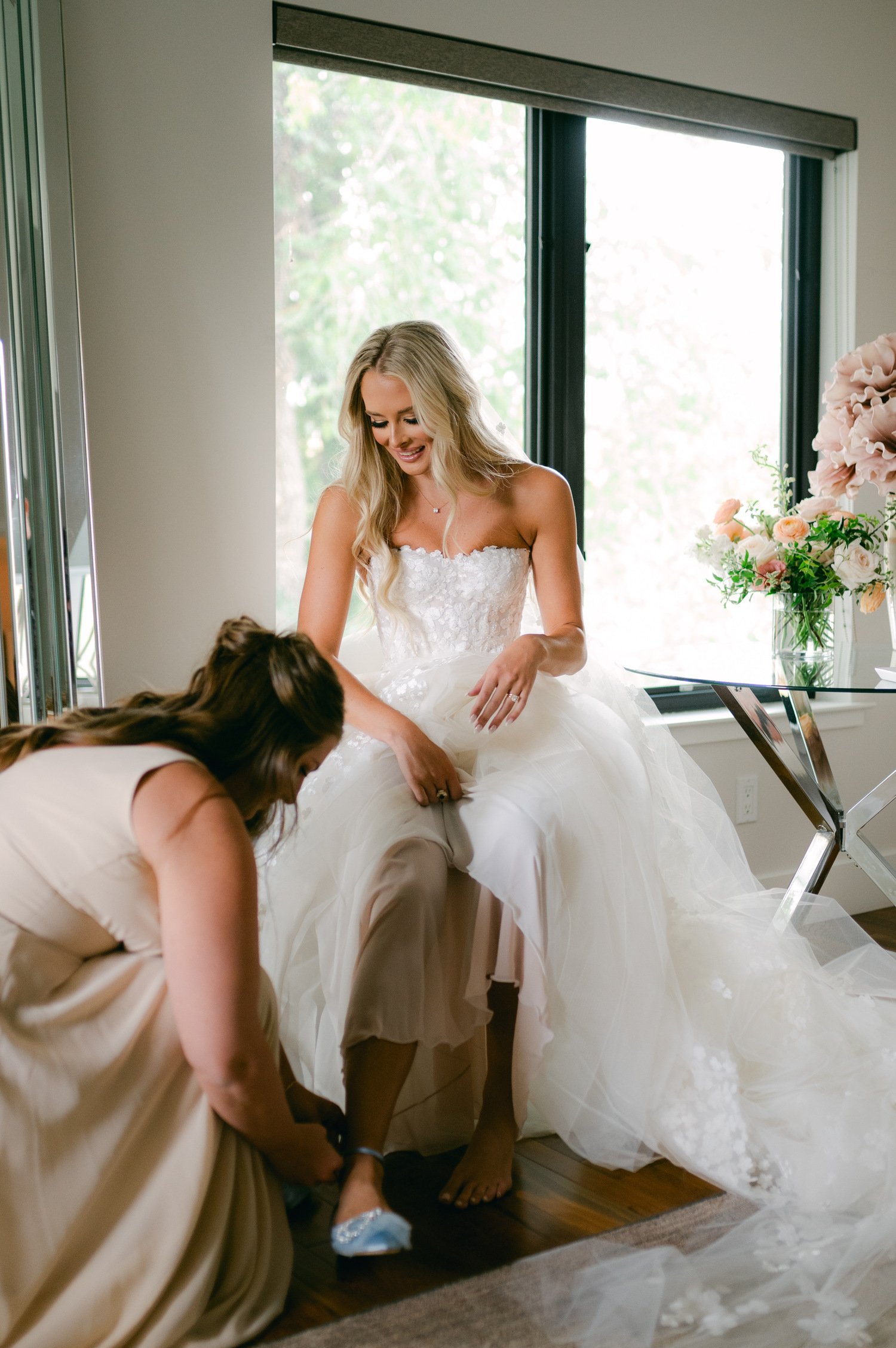 Elm Estate Wedding photos, photo of the maid of honor assisting the bride wear her blue wedding day shoes with bow-design details