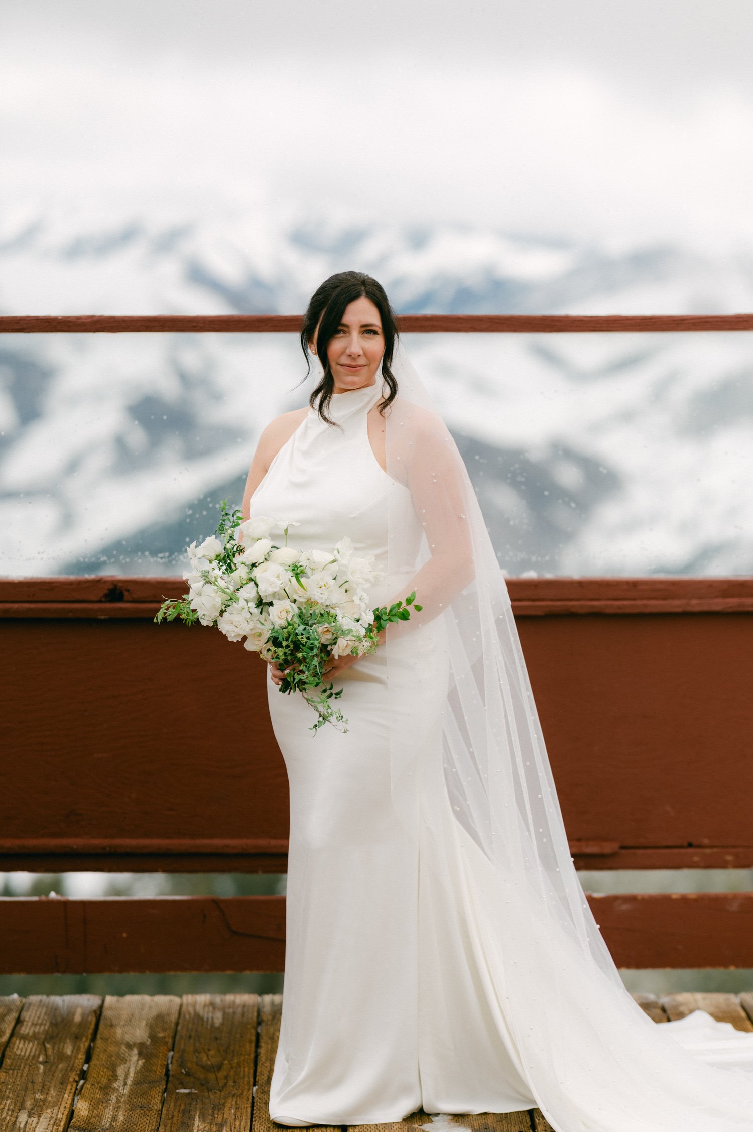 Sun Valley Roundhouse Wedding photos of the bride with her stunning wedding dress and long veil with pearl accents while holding her wedding bouquet with white flowers and greenery