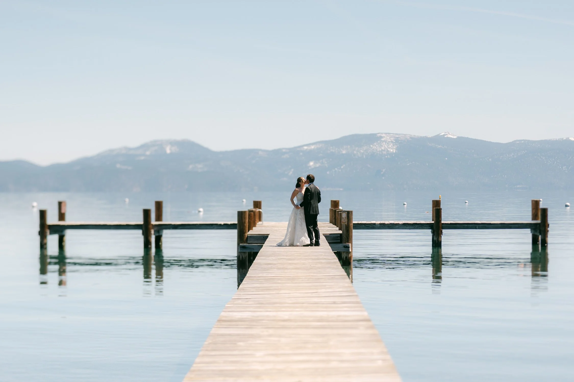 Palisades wedding venue, photo of intimate wedding first-look moment on a wooden pier overlooking a calm lake surrounded by snow-capped mountains. 