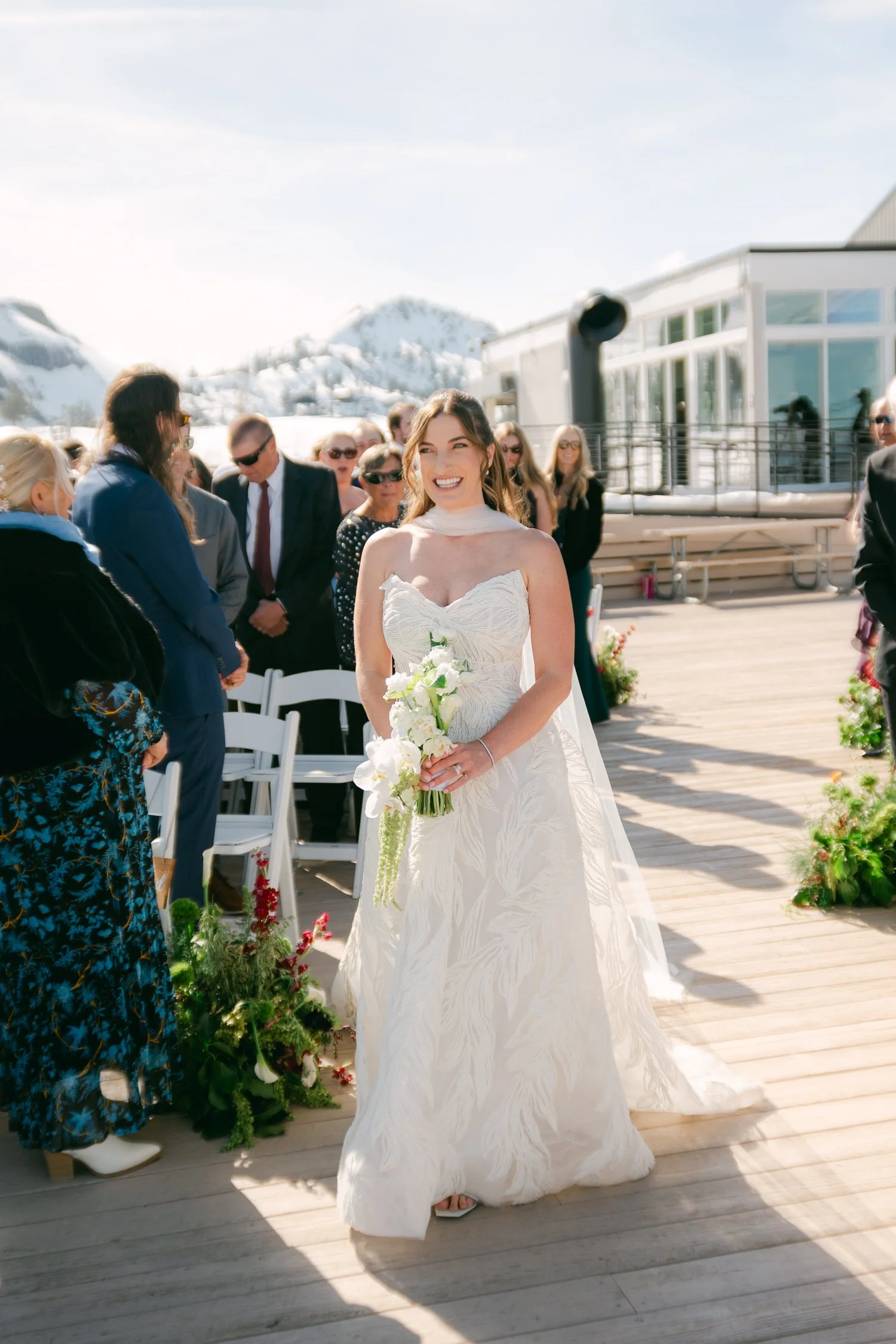 High Camp Ceremony, photo of the radiant bride wearing a structured white wedding gown with a delicate texture walking down the aisle