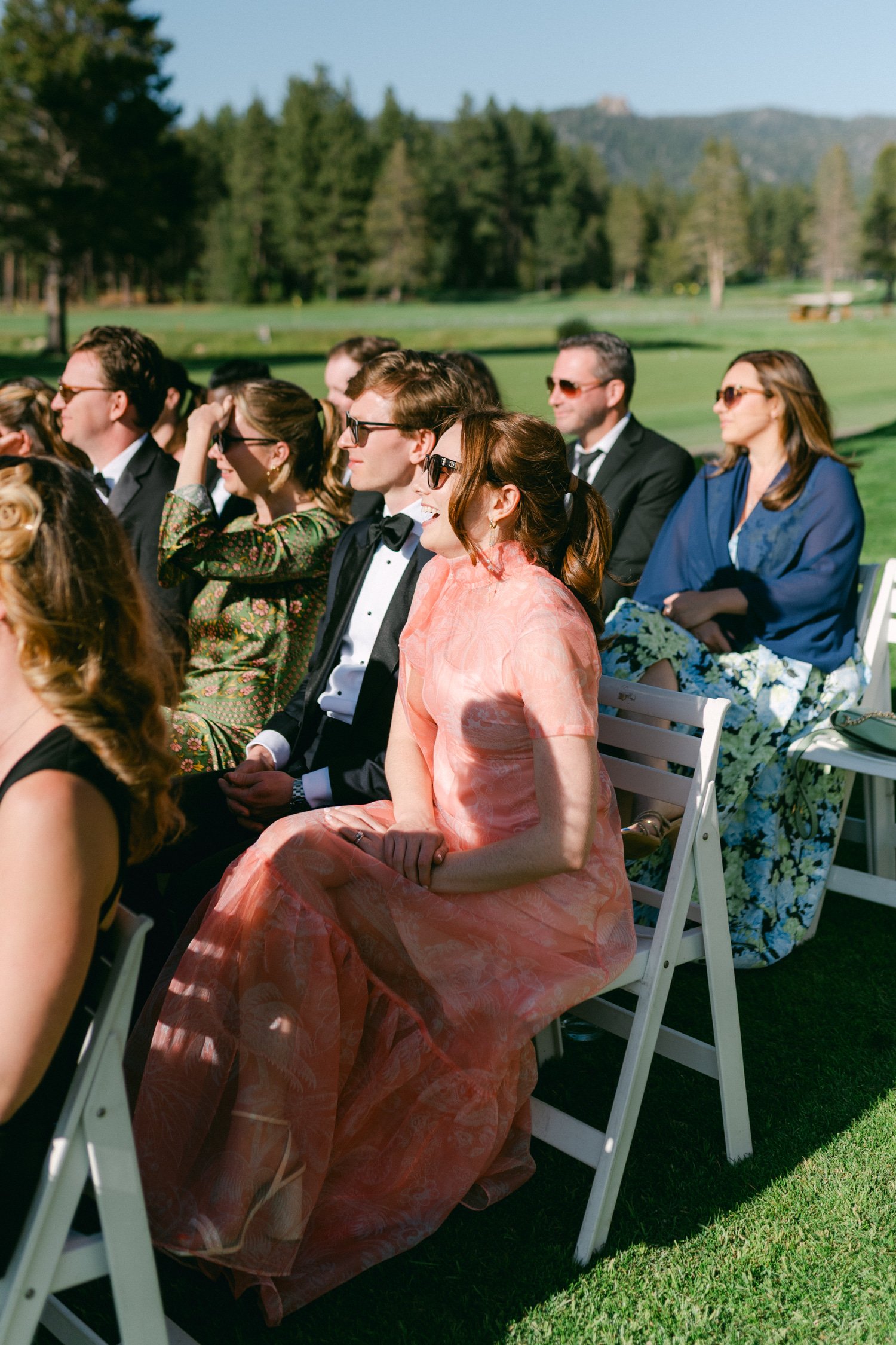Edgewood maximalist wedding, photo of a scenic outdoor wedding ceremony featuring stylish guests seated in white chairs on a grass lawn