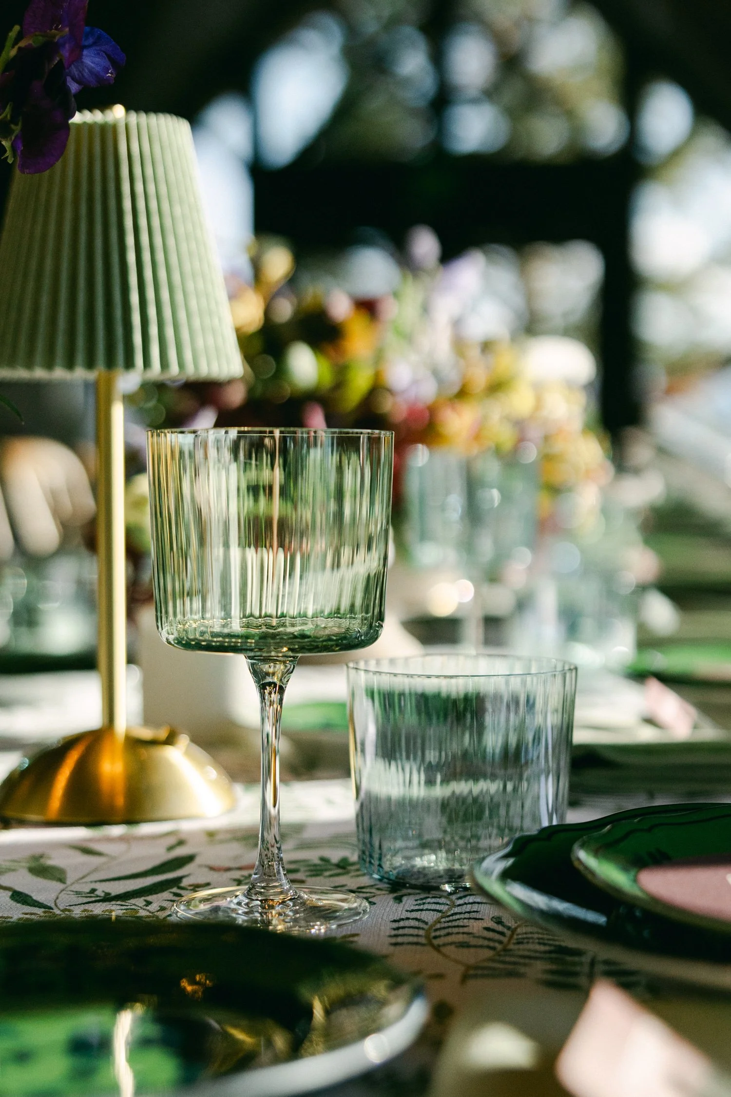 Edgewood maximalist wedding, photo of tablescape featuring a sophisticated design characterized by fluted glassware, rechargeable ambient lighting, and deep emerald accents.