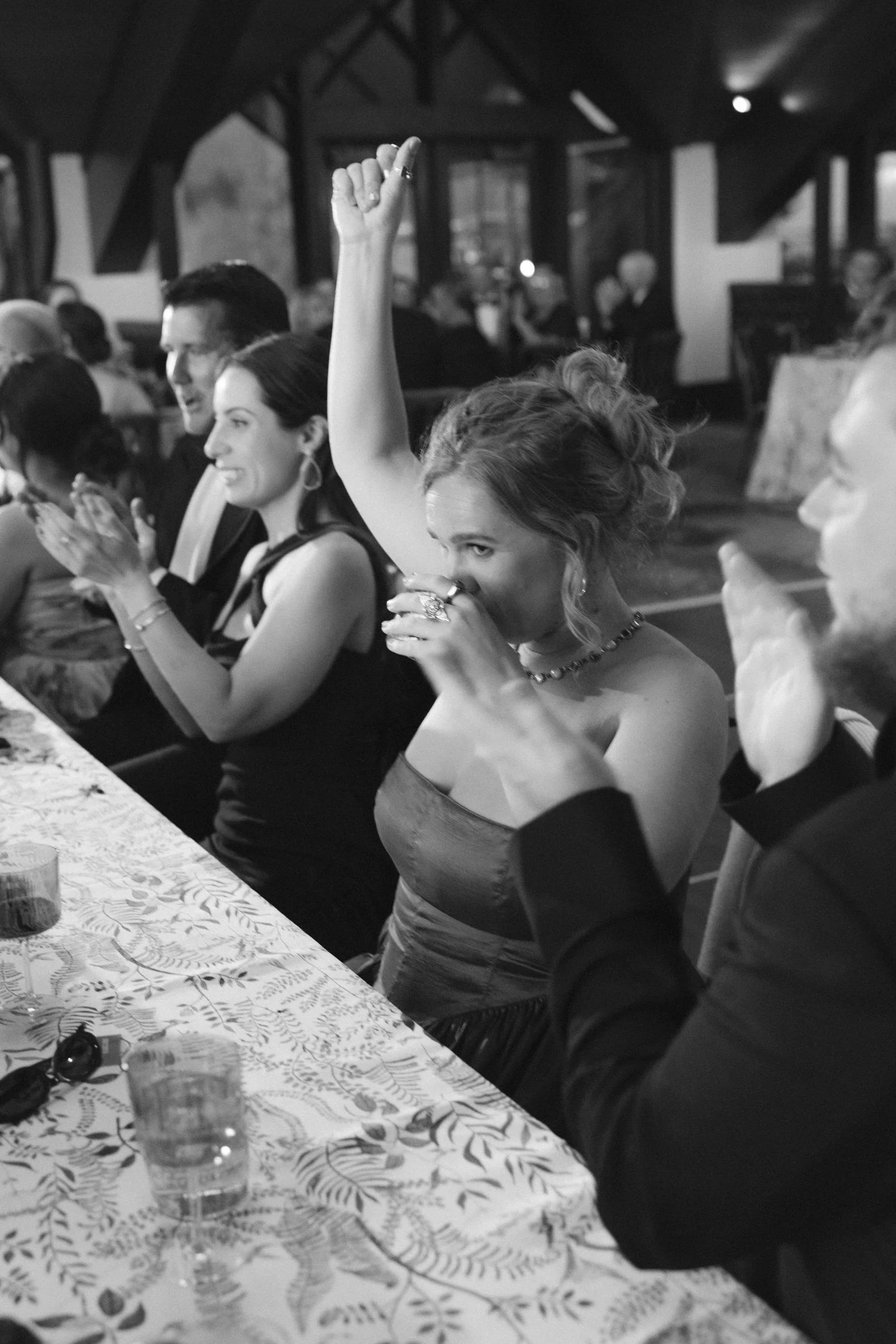 Edgewood maximalist wedding, photo of a lively wedding reception featuring guests enjoying dinner and celebrating with cheering and applause