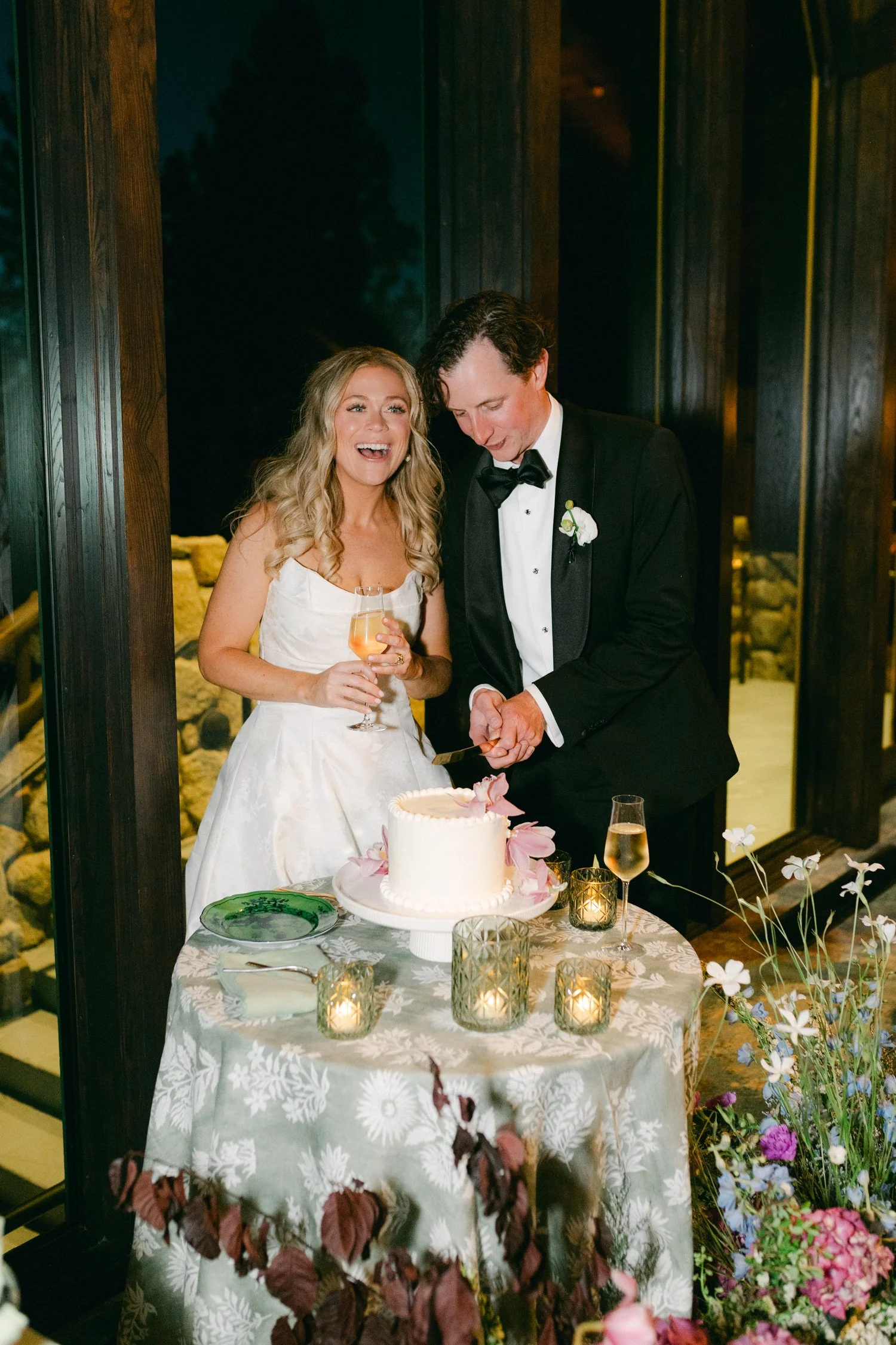 Edgewood maximalist wedding, photo of the newlywed couple cutting a simple white wedding cake adorned with delicate pink flowers at their reception.