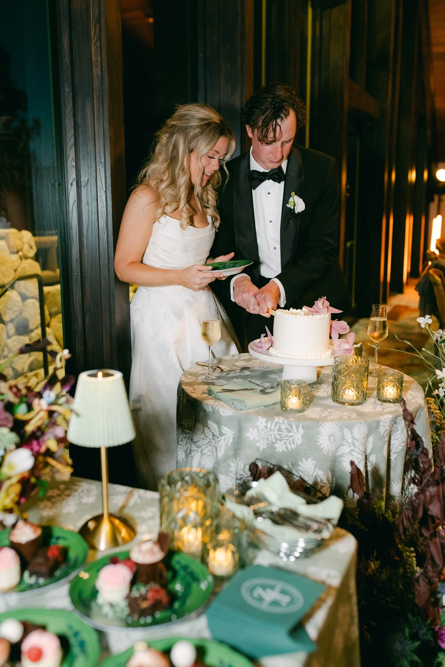 Edgewood maximalist wedding, photo of the newlyweds cutting their wedding cake, which is decorated with pink and white floral accents 