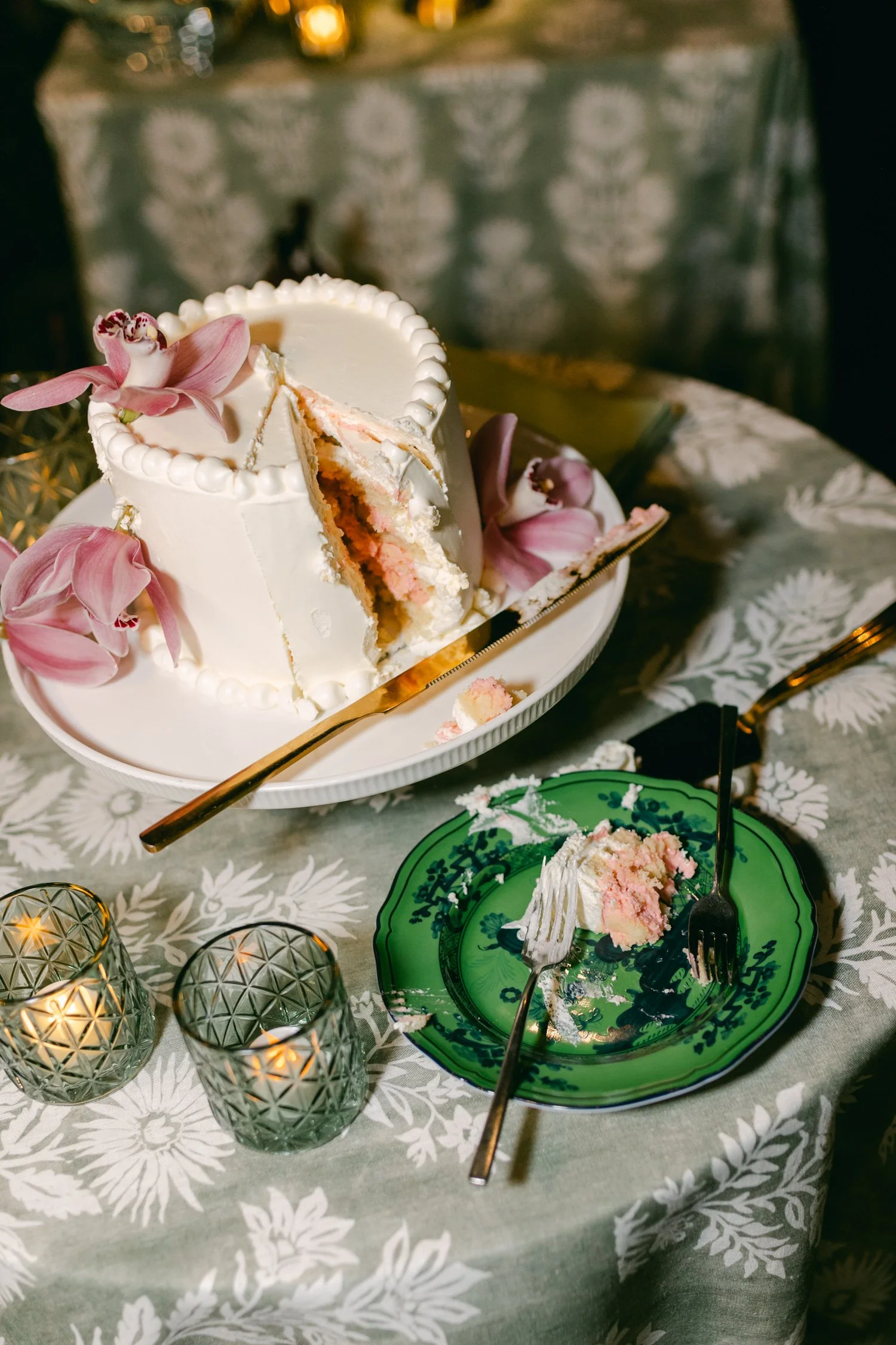Edgewood maximalist wedding, photo of a white wedding cake decorated with fresh pink flowers and a green patterned tablecloth.