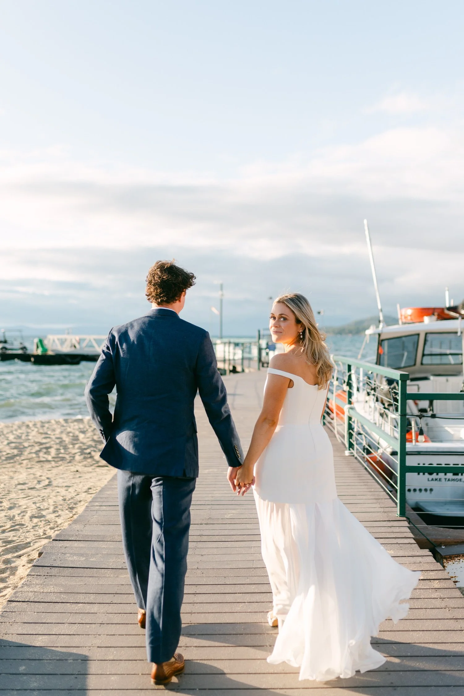 Riva Grill welcome party, photo of the couple walking on a wooden dock overlooking the waterfront, with boats and sandy beaches