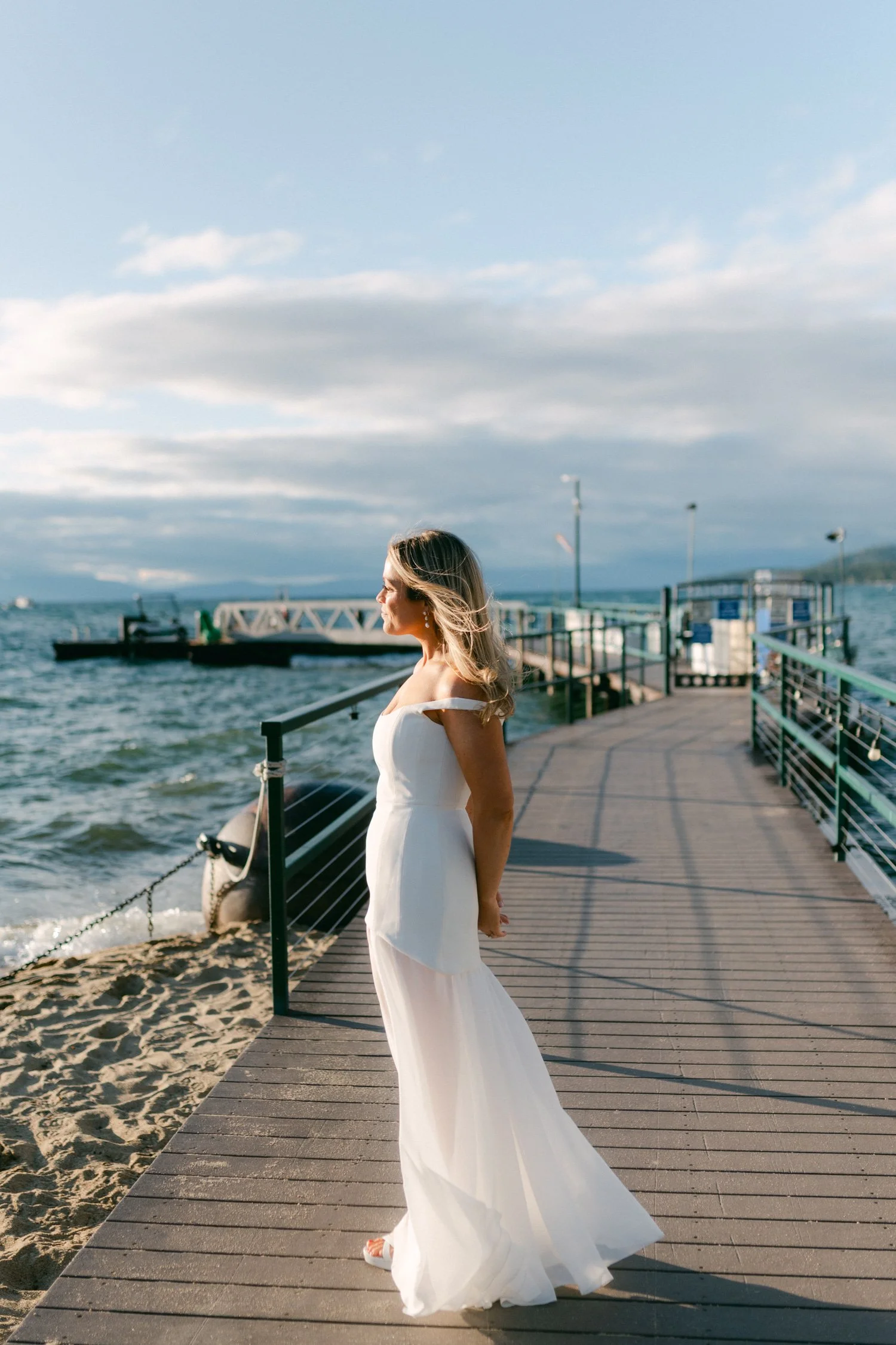Riva Grill welcome party, photo of the bride standing on a wooden dock in a sophisticated off-the-shoulder neckline and flowing satin draping dress