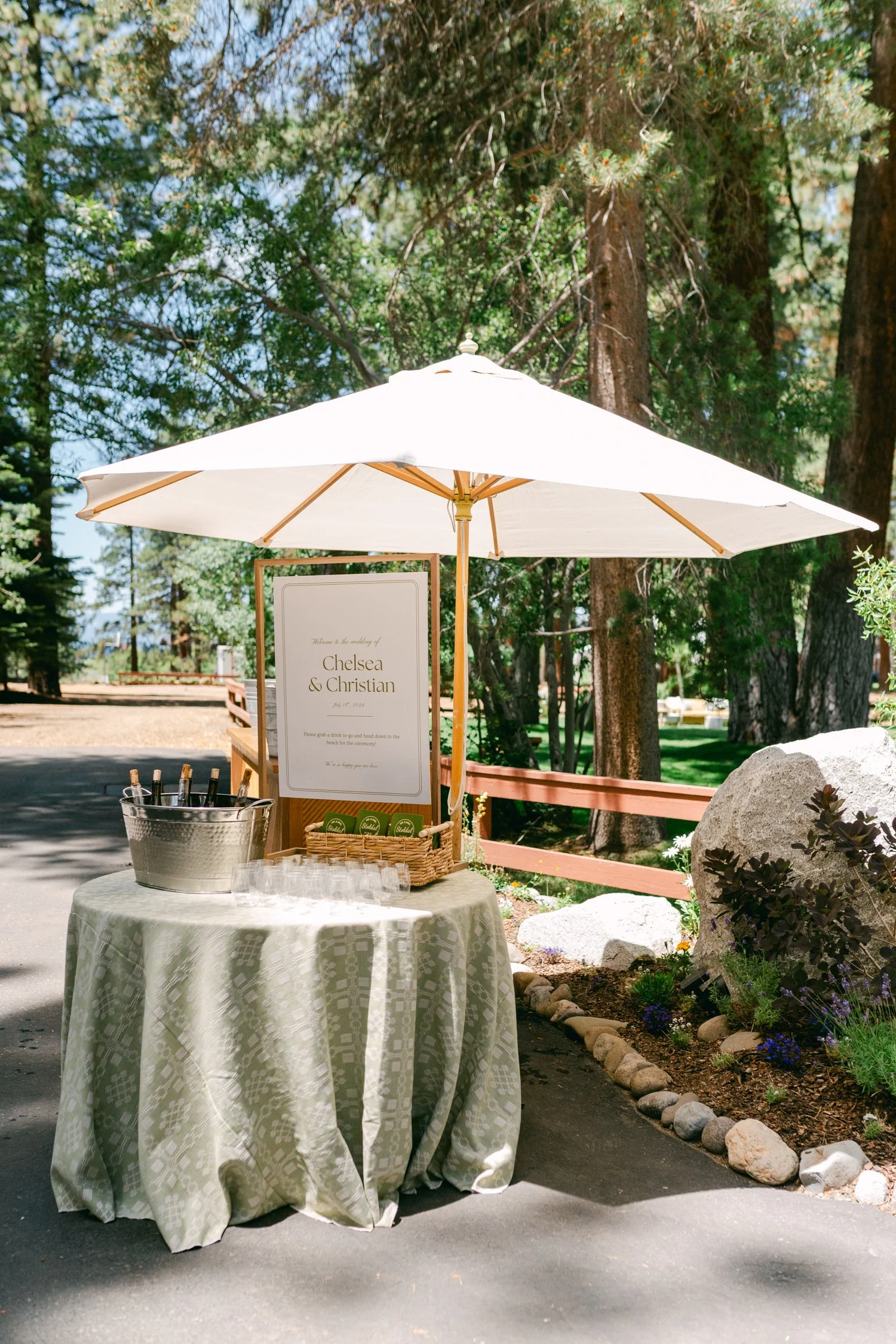 Lake Tahoe 4-H Camp wedding photos, photo of outdoor wedding welcome station with a white parasol for shade and a light green patterned tablecloth.