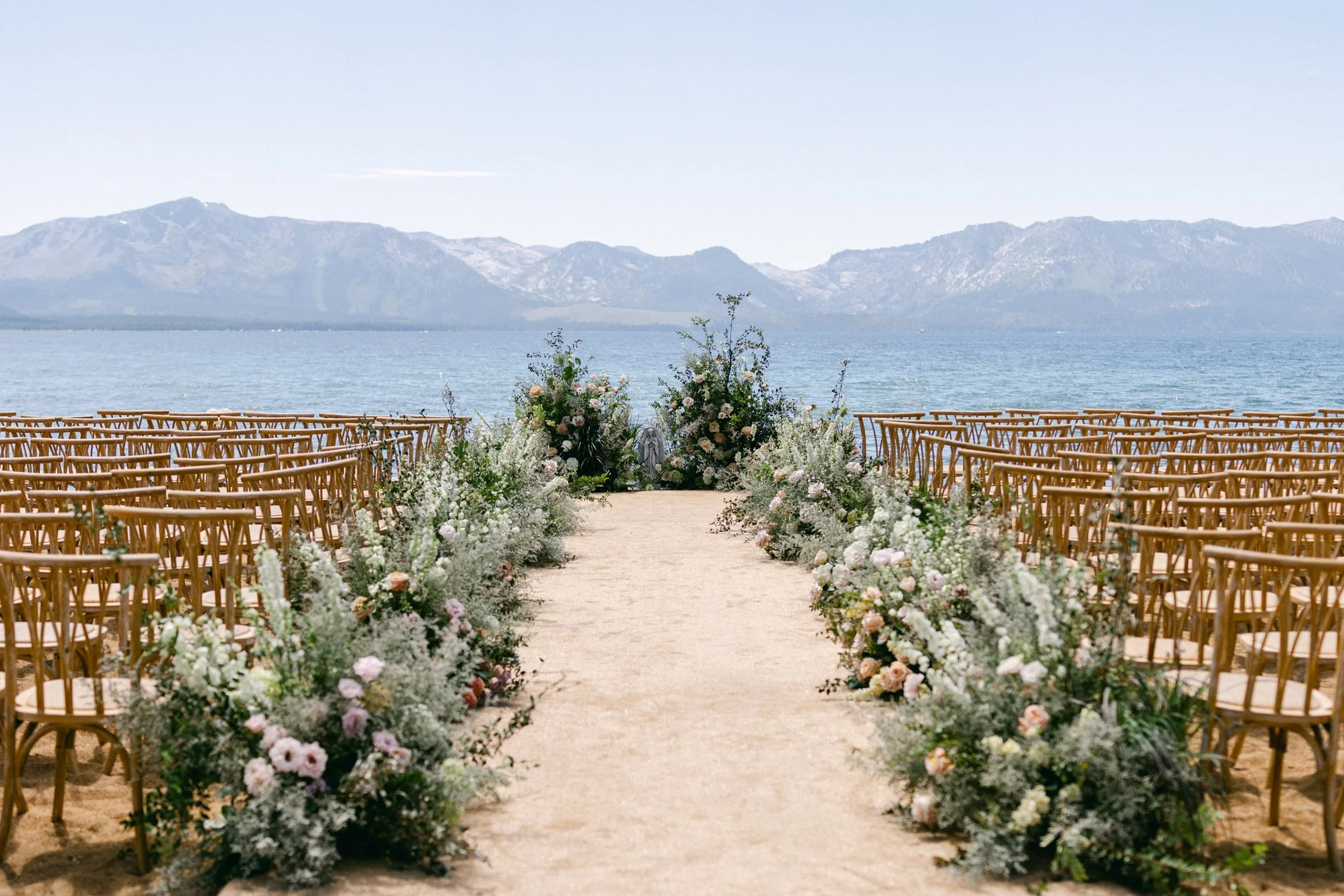 Lake Tahoe 4-H Camp wedding photos, photo of lakeside wedding ceremony set up featuring rustic-style wooden chairs arranged along a sandy aisle 