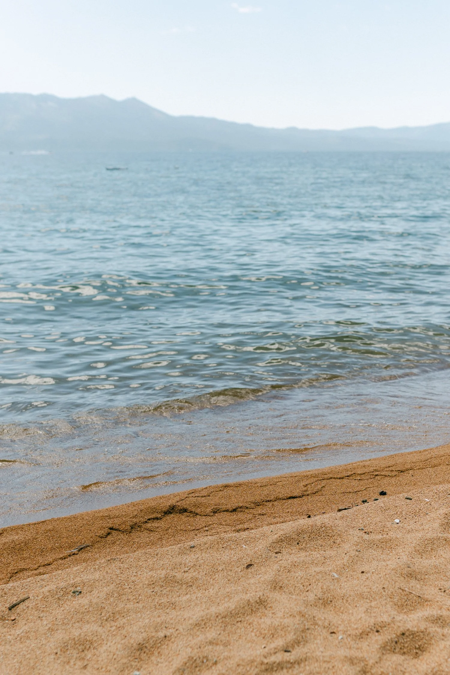 Lake Tahoe 4-H Camp wedding photos, photo of a sandy beach shoreline with clear blue water and hazy mountains in the distant background