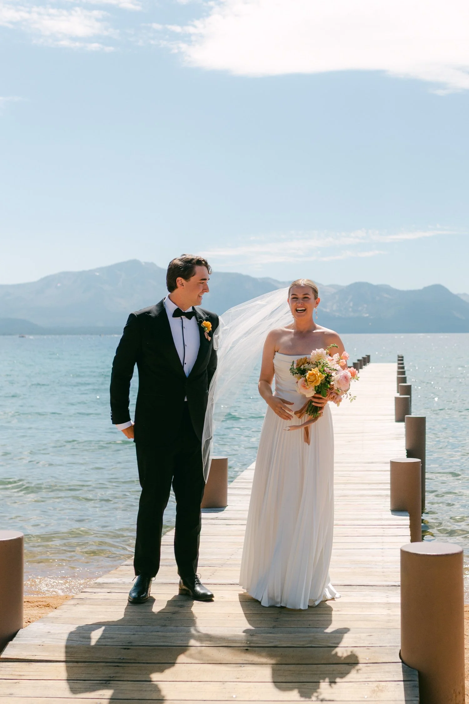 Lake Tahoe 4-H Camp wedding photos, photo of the newlyweds standing on a wooden pier overlooking a large lake surrounded by mountains