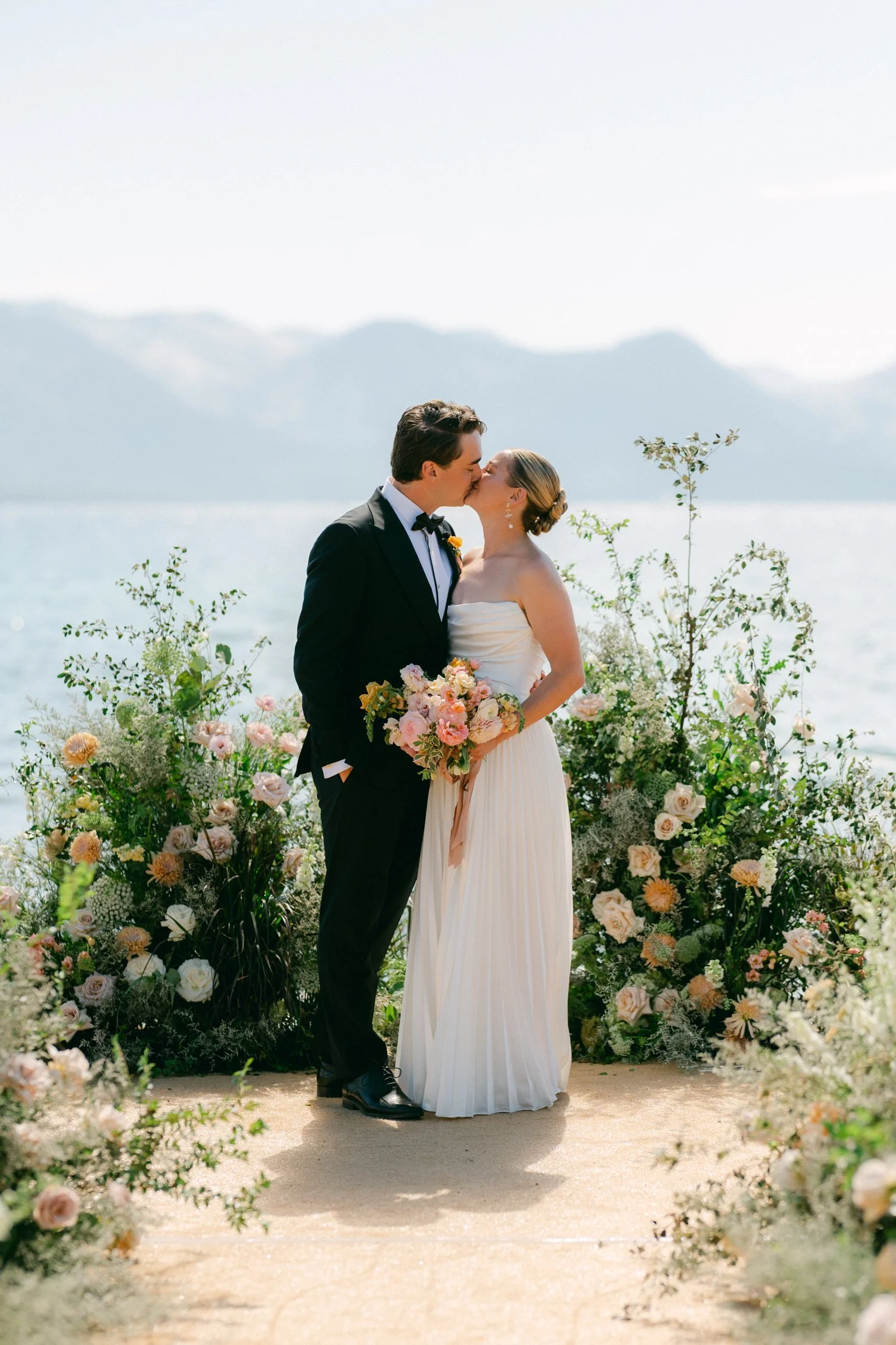 Lake Tahoe 4-H Camp wedding photos, photo of the newlyweds in a serene, lake-side ceremony featuring a stunning, asymmetrical floral backdrop with spring florals