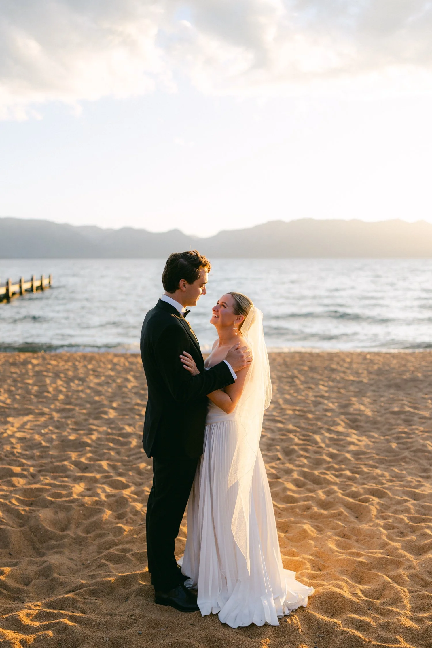 Lake Tahoe 4-H Camp wedding photos, photo of the couple standing on a sandy shore at sunset with Lake Tahoe in the background