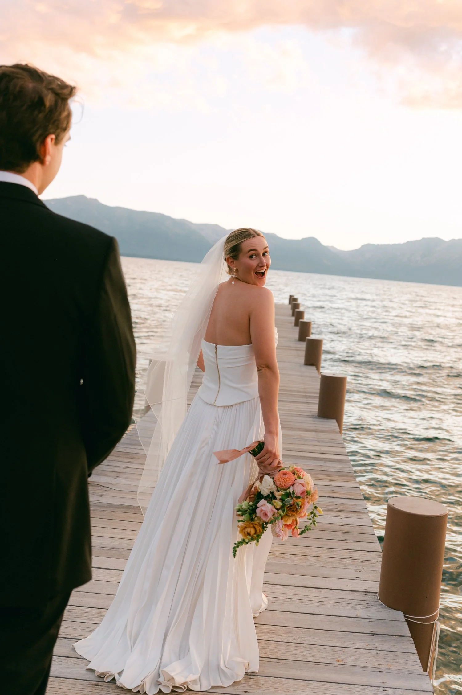 Lake Tahoe 4-H Camp wedding photos, photo of the couple captured in a candid, joyful moment on a wooden dock overlooking a lake.