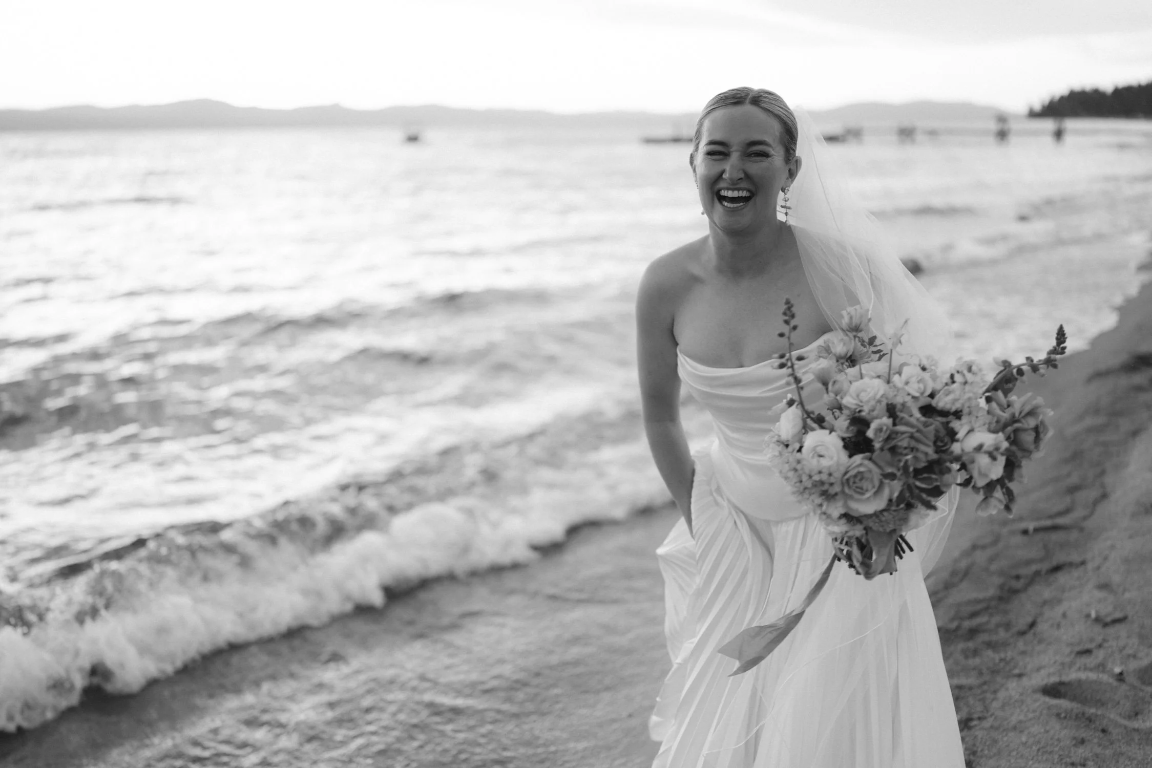 Lake Tahoe 4-H Camp wedding photos, photo of the blissful bride in a modern, strapless gown with draped fabric and a flowing skirt, paired with a simple veil by the lakeside