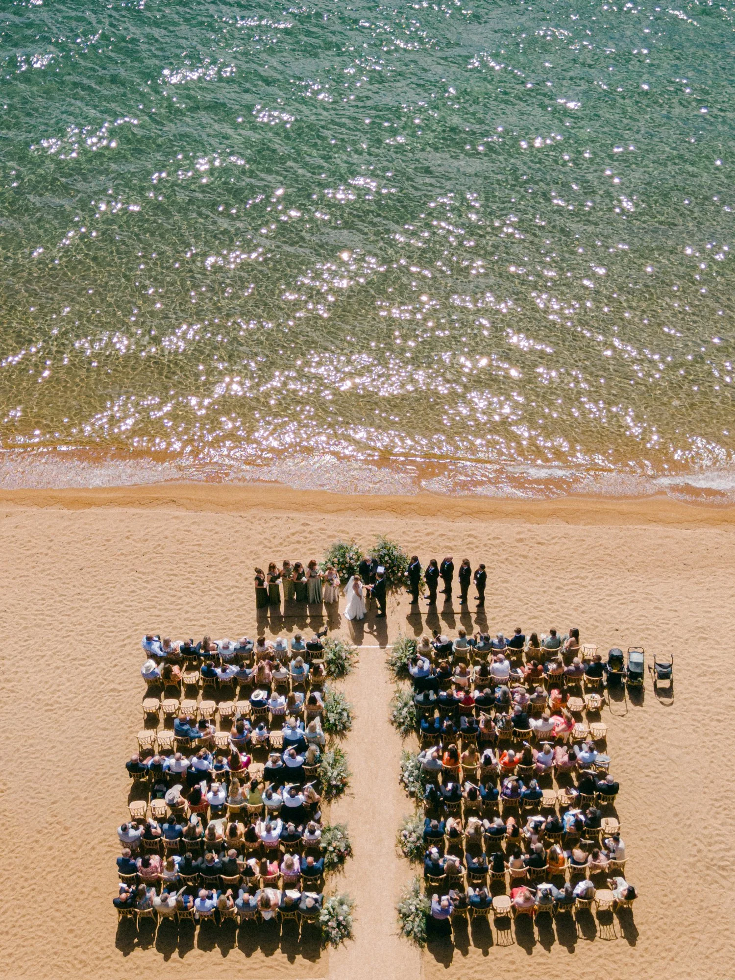 Lake Tahoe 4-H Camp wedding photos, photo of a scenic aerial view of a beach wedding ceremony featuring guests seated in chairs arranged on the sand