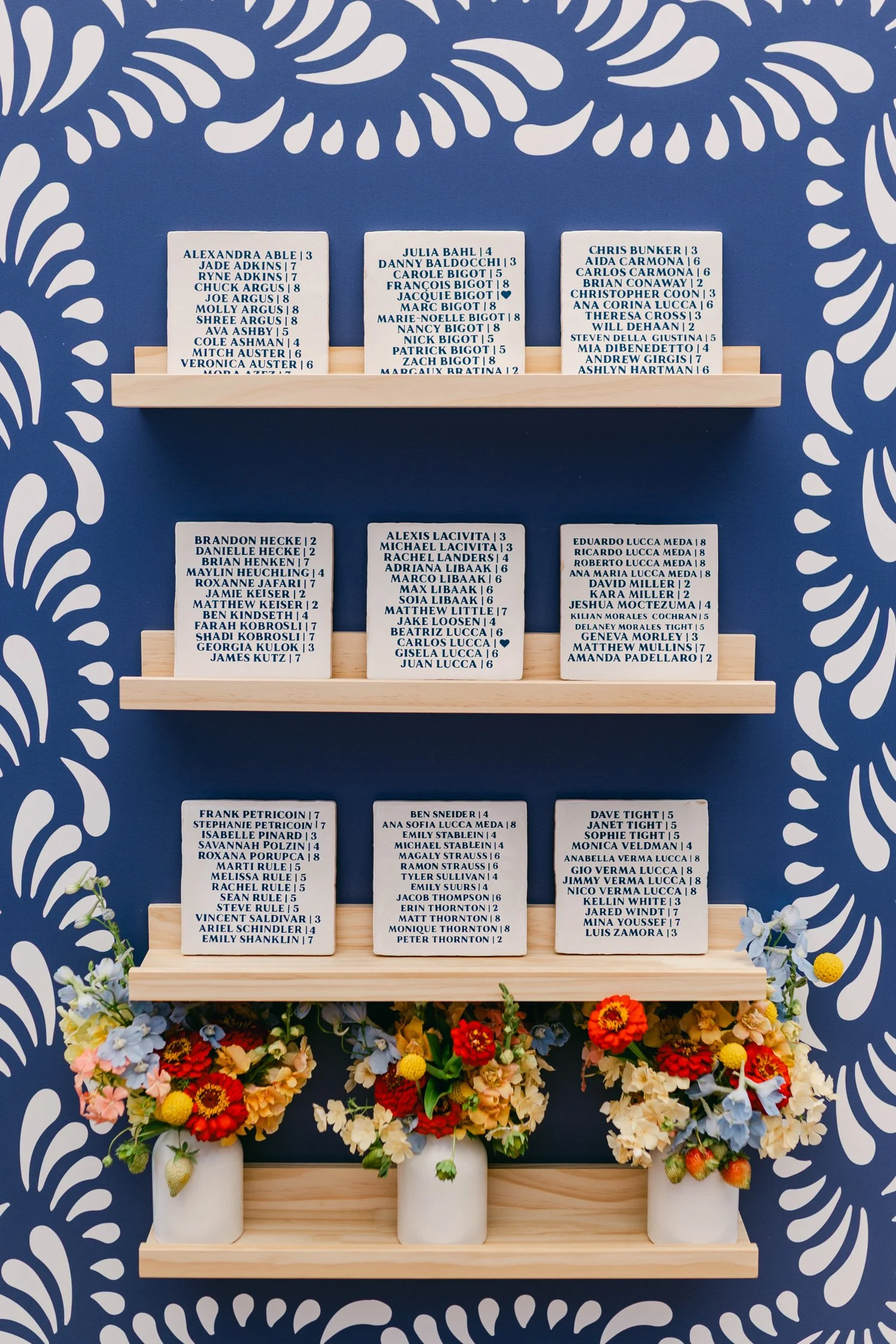 Zephyr Lodge wedding, photo of custom seating plan installation features hand-painted tiles arranged on wooden shelves against a dramatic blue and white patterned wallpaper.
