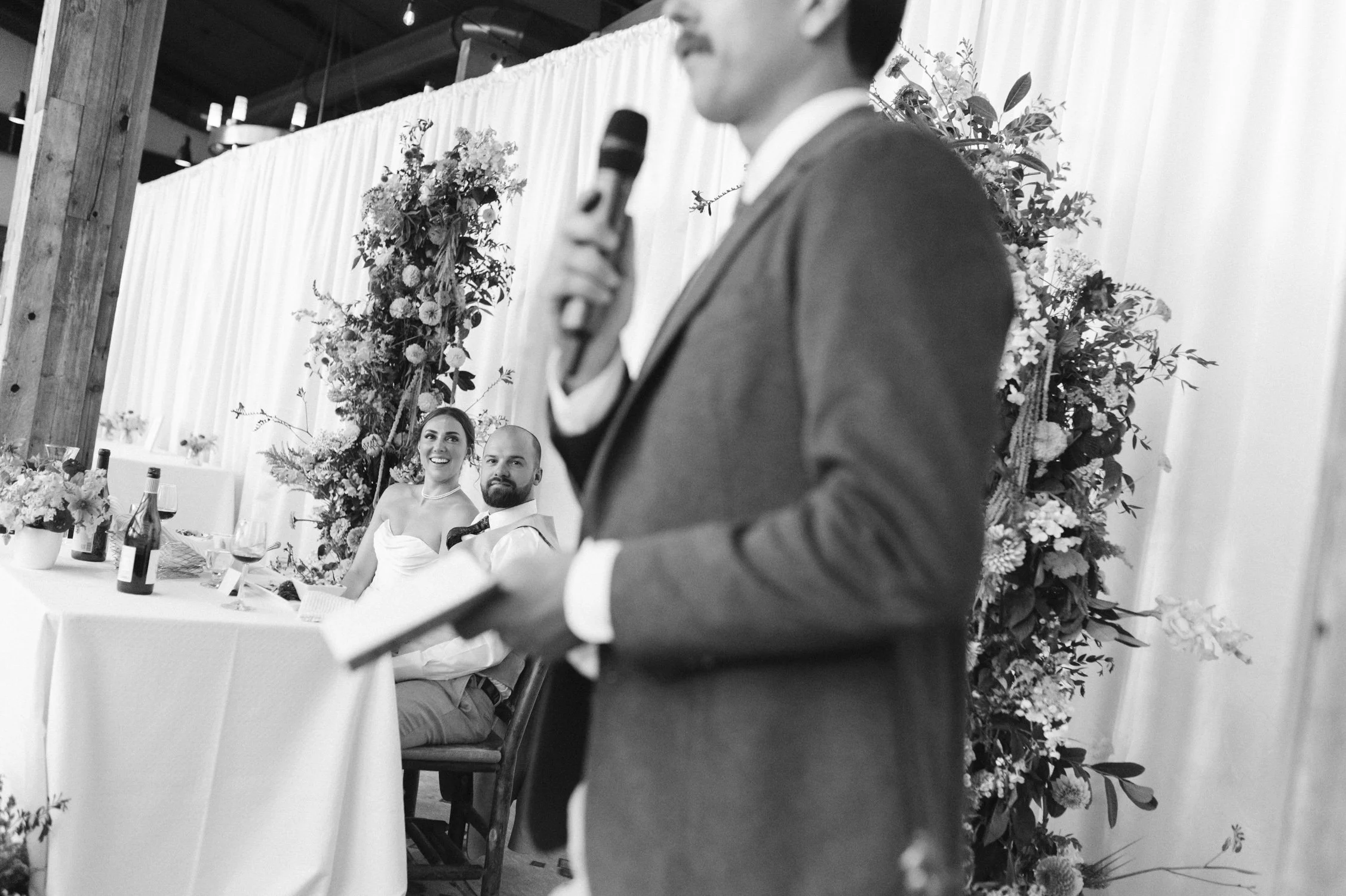 Zephyr Lodge wedding, photo of the couple smiling at a wedding reception while someone gives a speech