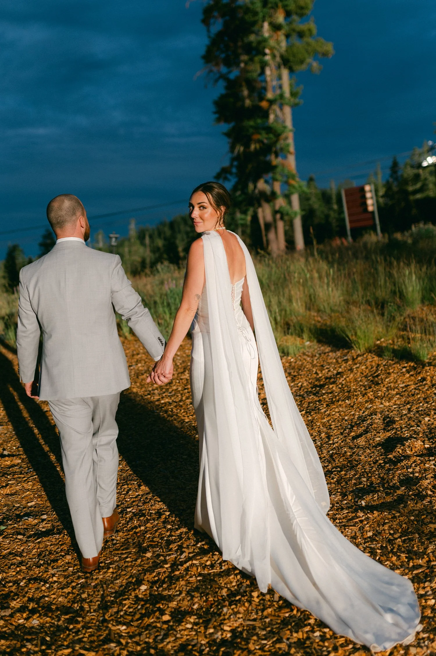 Zephyr Lodge wedding, photo of the bride and groom walking with the bride wearing a sleek white wedding gown with a dramatic flowing chiffon cape