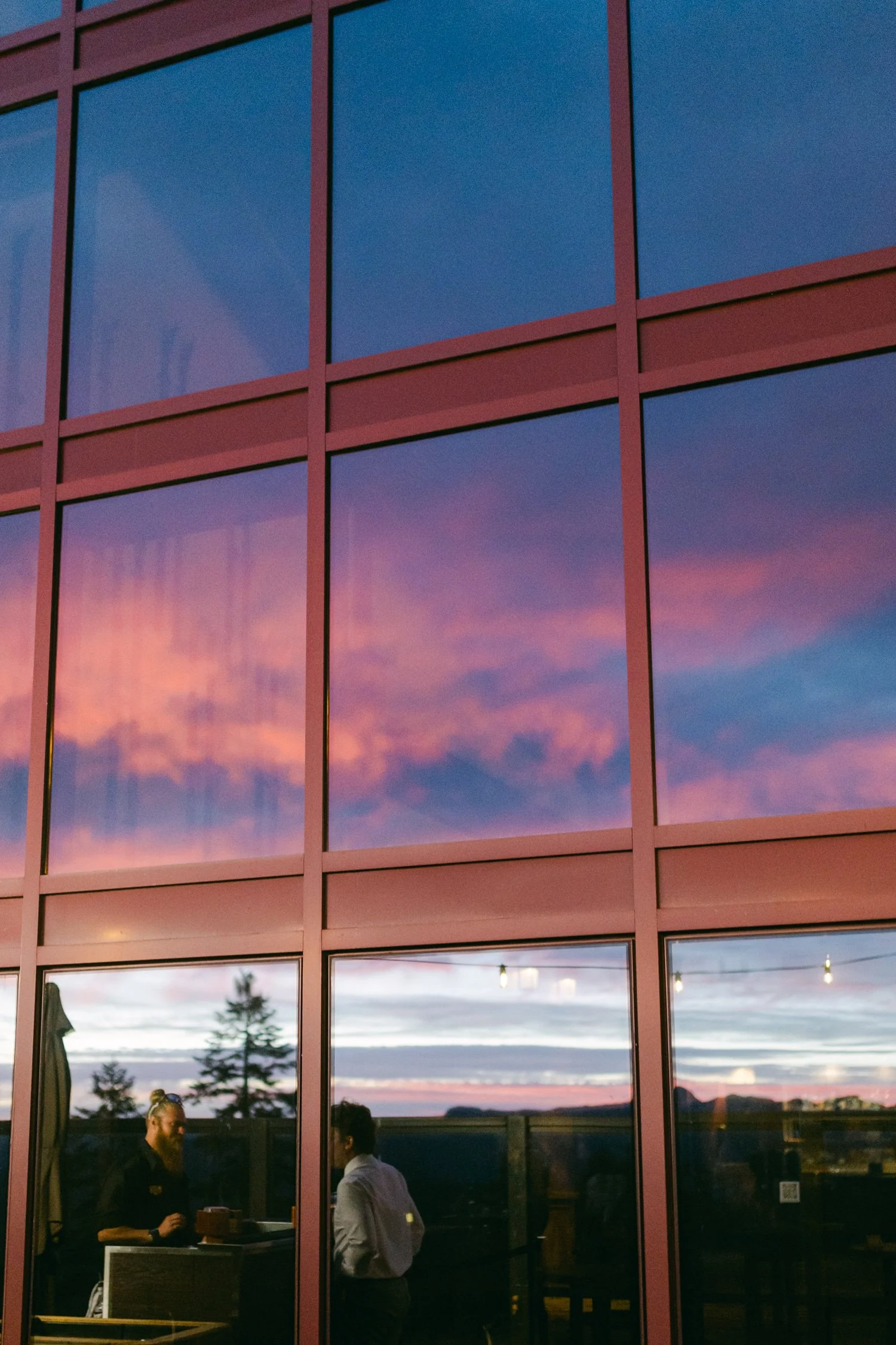 Zephyr Lodge wedding, photo of glass windows that vividly reflect a vibrant pink and orange sunset sky.