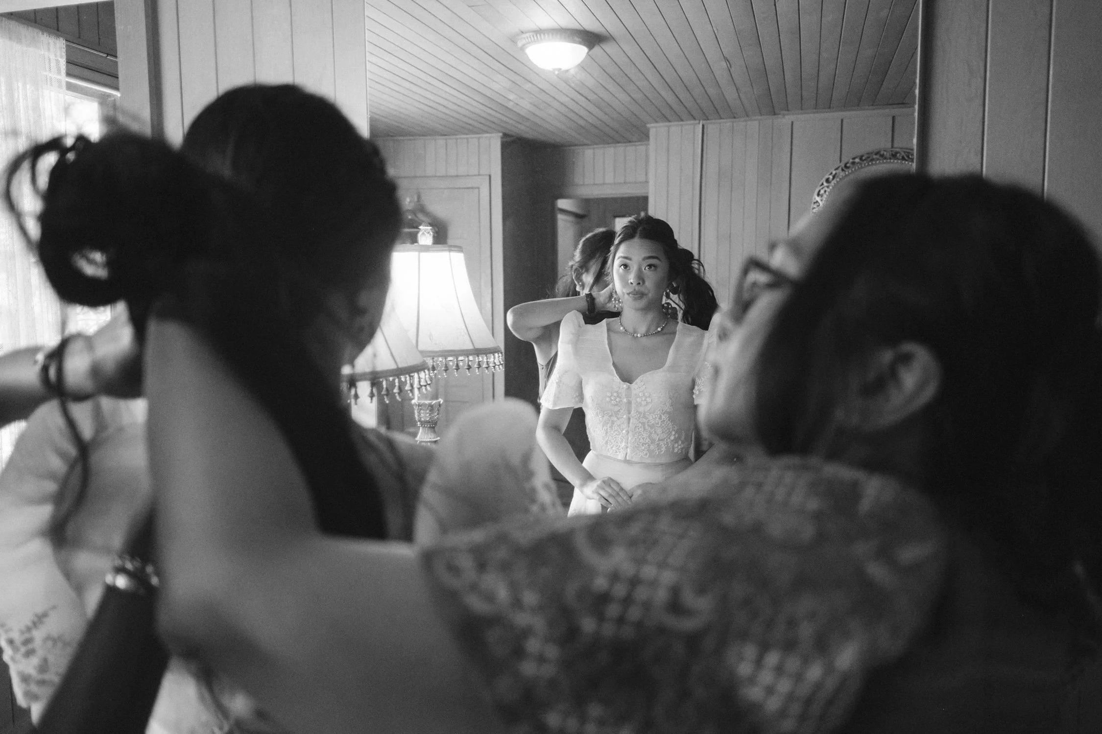 A Valhalla Lake Tahoe Wedding, photo of the bride getting ready in a mirror reflection while surrounded by people helping with her hair and dress.