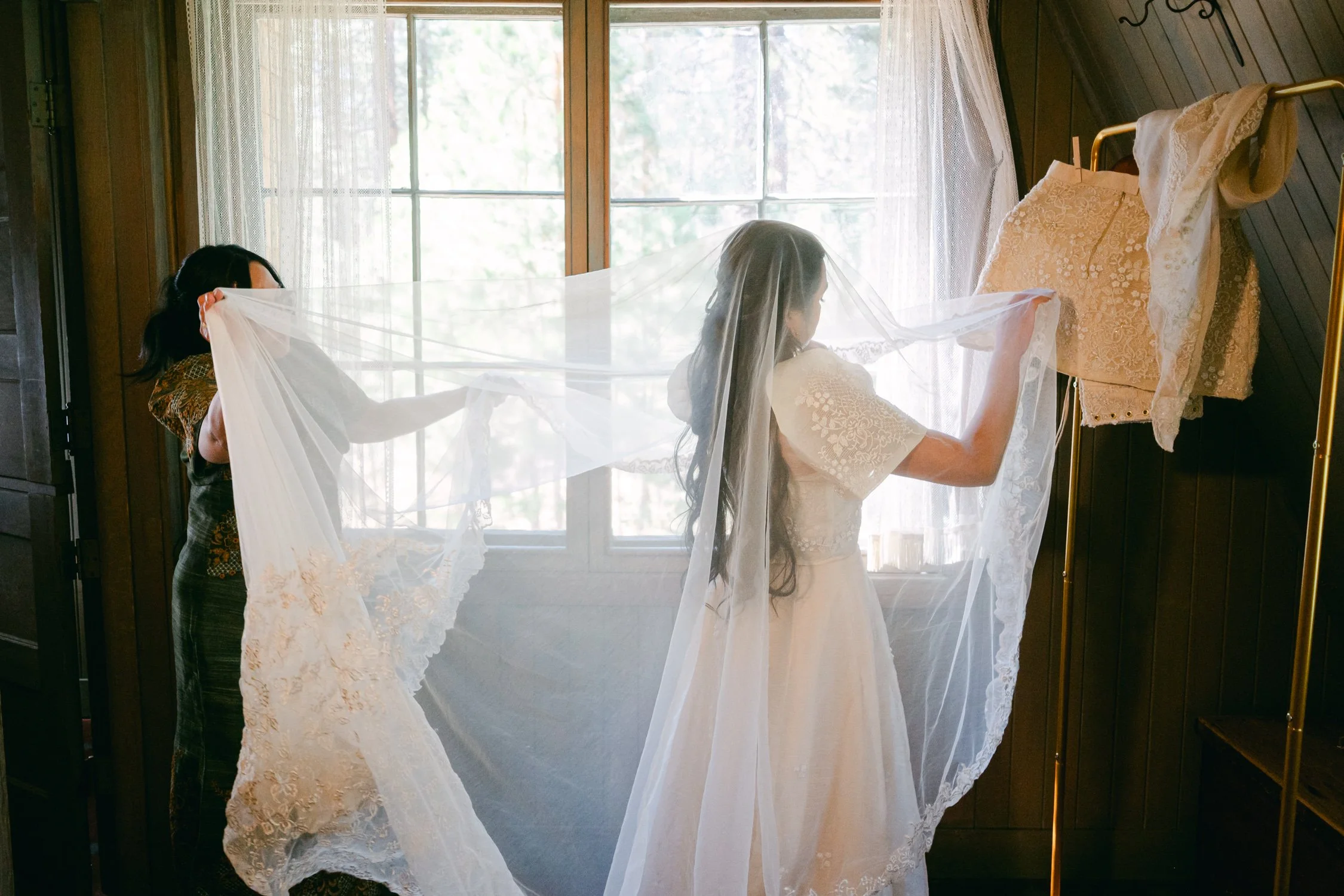 A Valhalla Lake Tahoe Wedding, photo of the bride trying on a long, sheer lace-trimmed wedding veil by a sunlit window