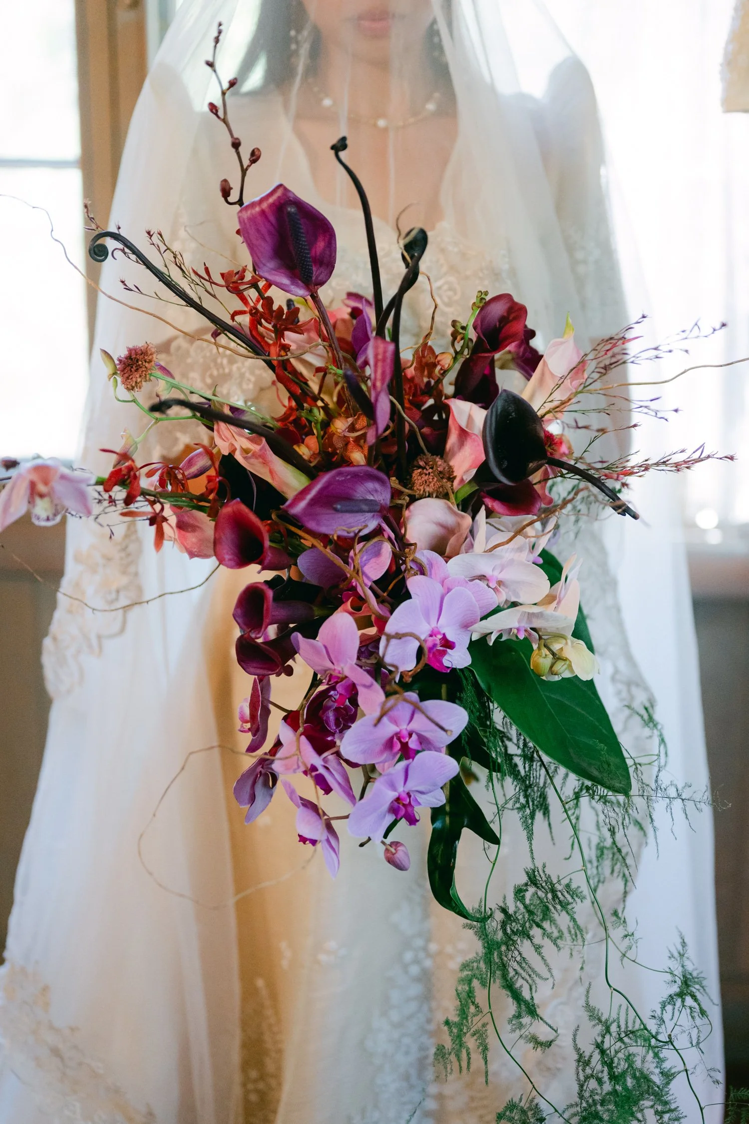 A Valhalla Lake Tahoe Wedding, photo of dramatic cascading bridal bouquet featuring vibrant purple and pink orchids paired with deep burgundy calla lilies and dark anthuriums
