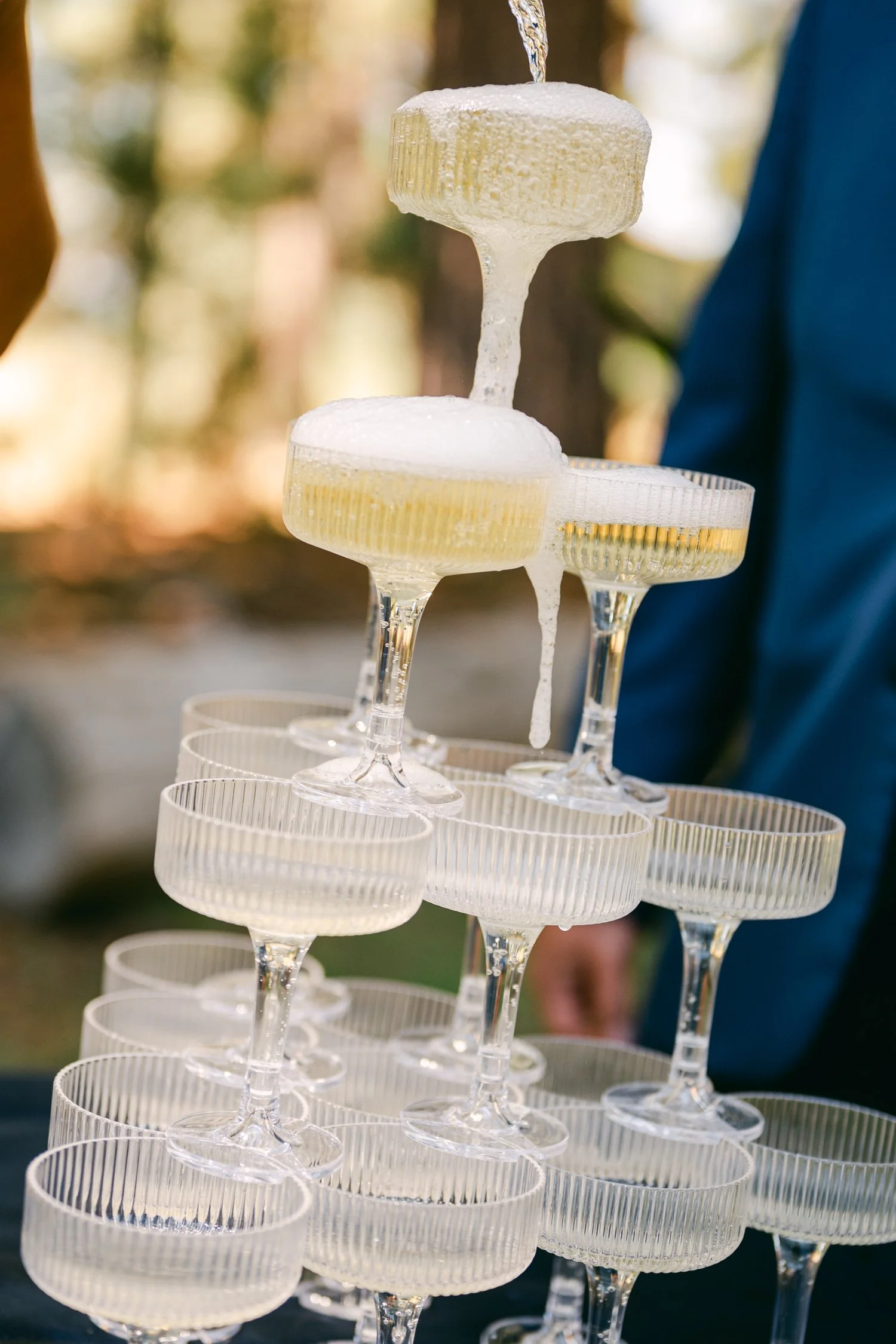 A Valhalla Lake Tahoe Wedding, photo of a classic champagne tower being poured, featuring stacked, vertical-ribbed coupe glasses
