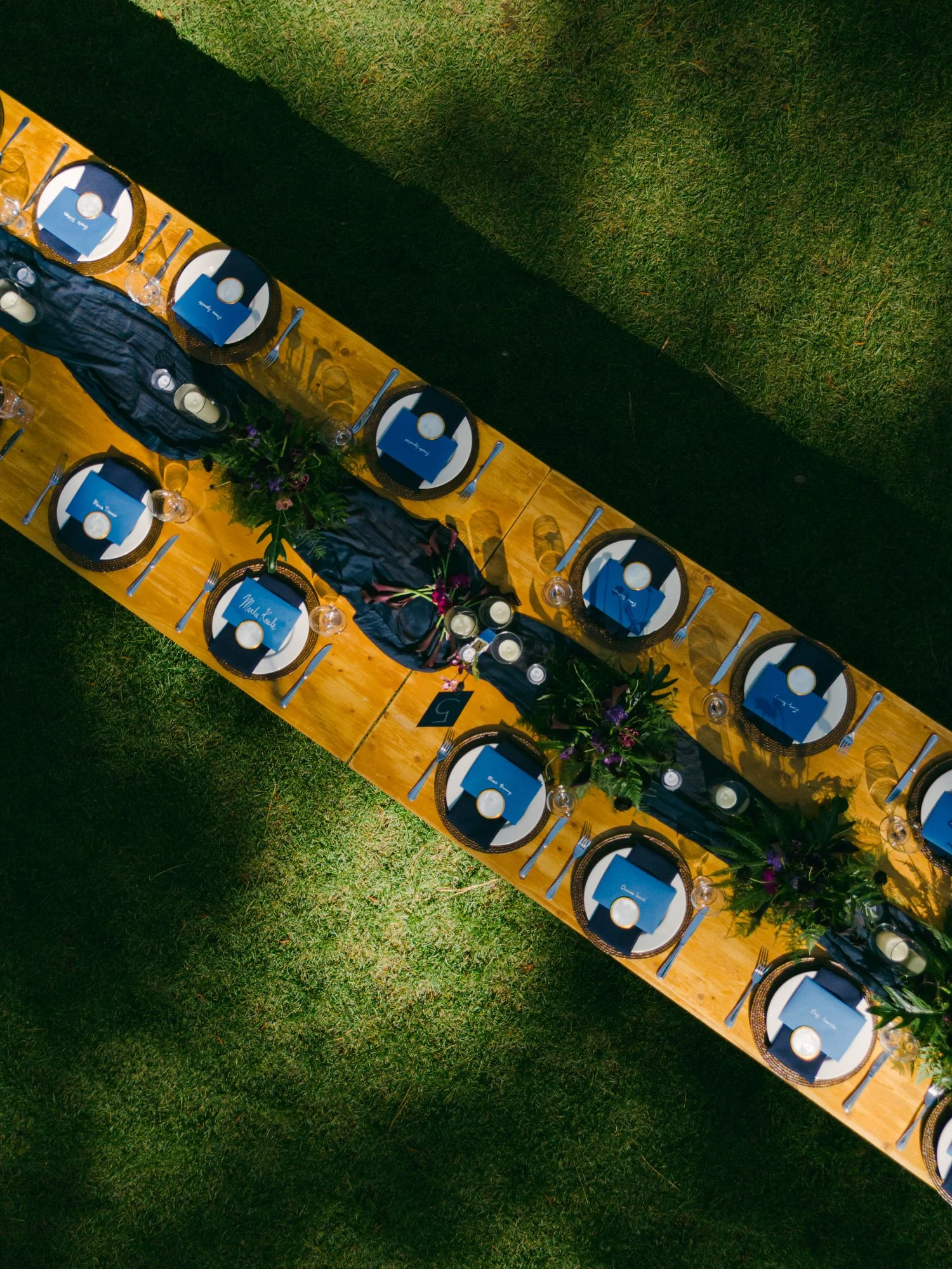 A Valhalla Lake Tahoe Wedding, photo of an aerial view showing an elongated rustic wooden banquet table set up outdoors on a green lawn for a special event or reception.