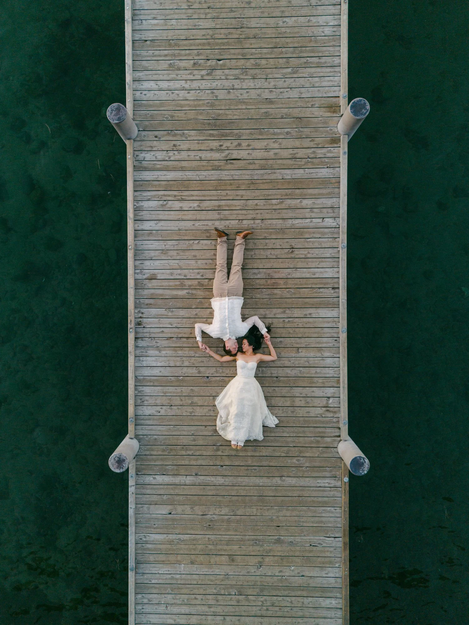 A Valhalla Lake Tahoe Wedding, photo of an overhead drone photograph of the bride and groom lying head-to-head on a long wooden dock over dark water.