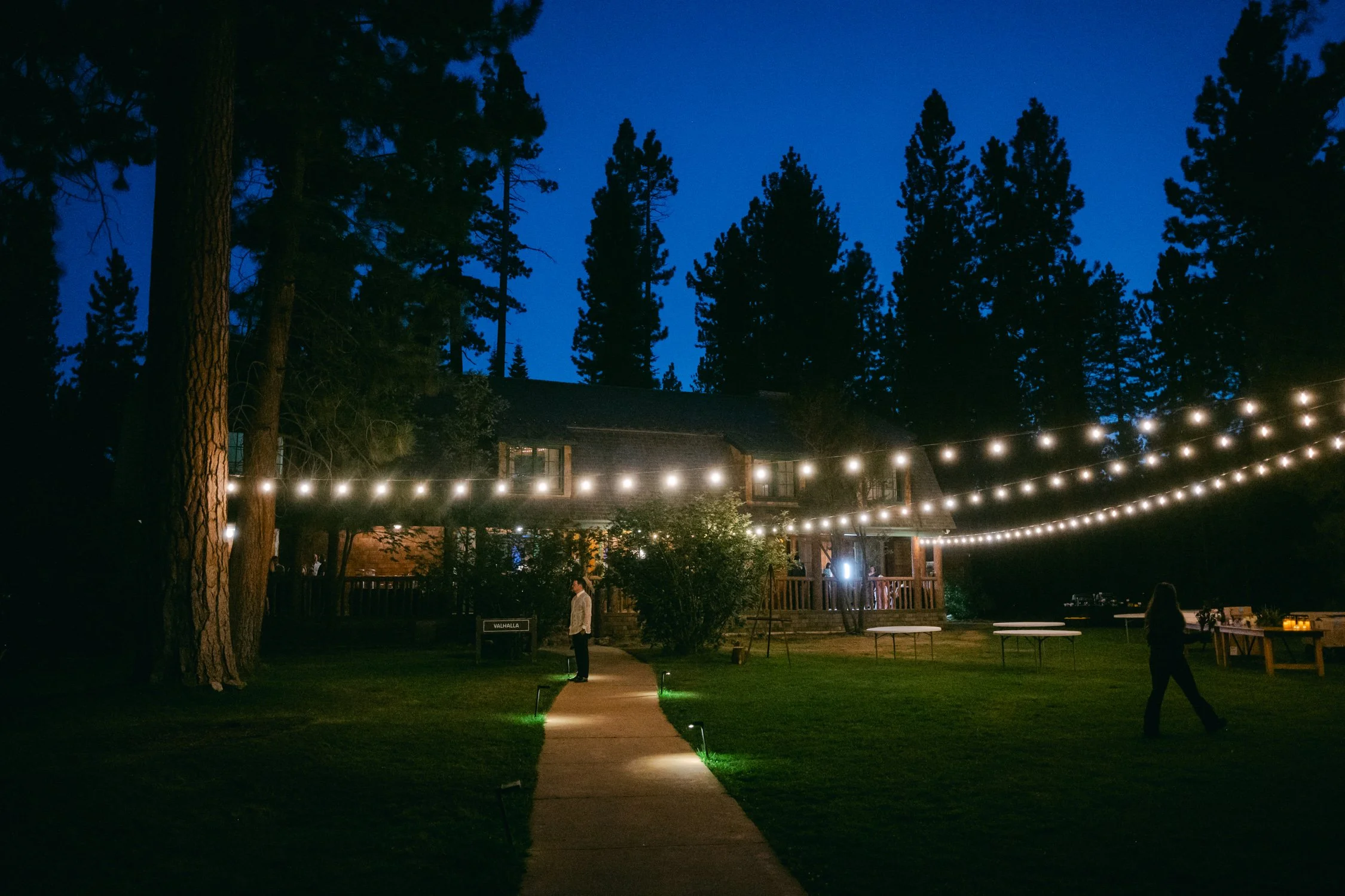 A Valhalla Lake Tahoe Wedding, photo of wedding reception venue set outdoors among pine trees, illuminated by string lights